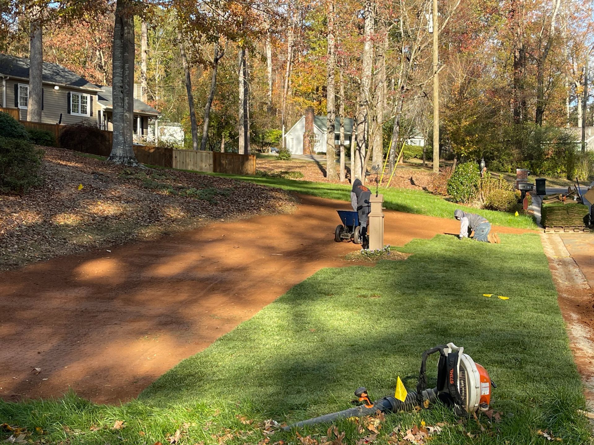 A man is working on a lush green lawn next to a dirt road.