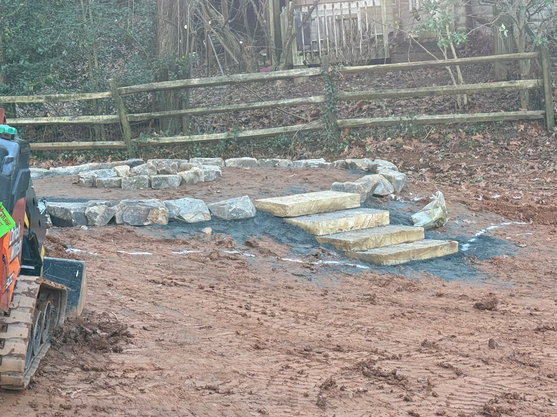 A bulldozer is moving dirt in a field next to a wooden fence.