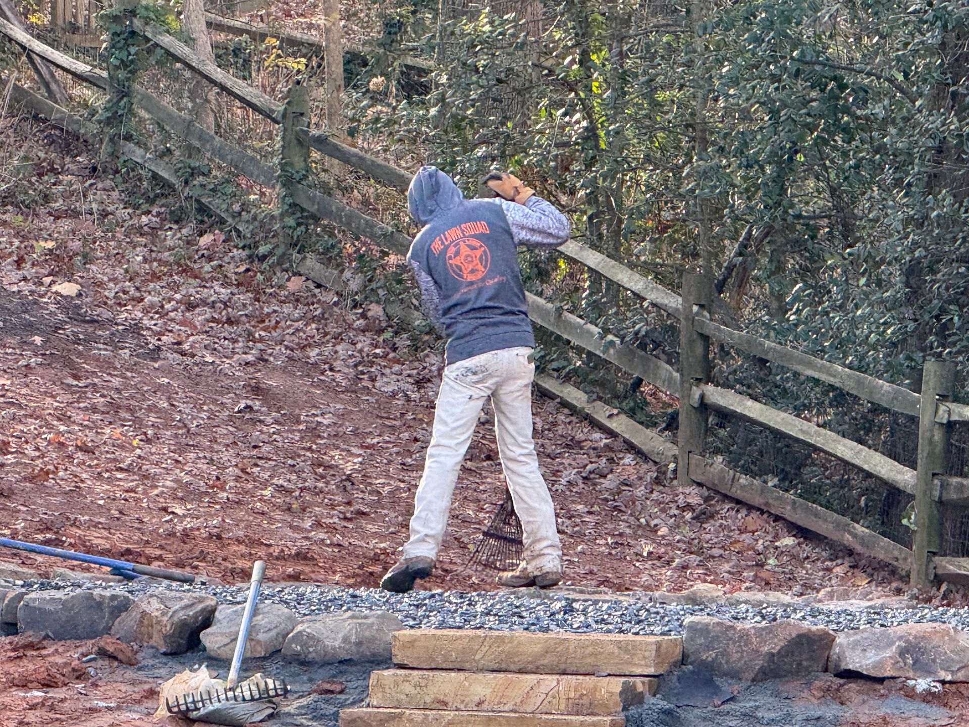 A man in a hoodie is standing next to a wooden fence.