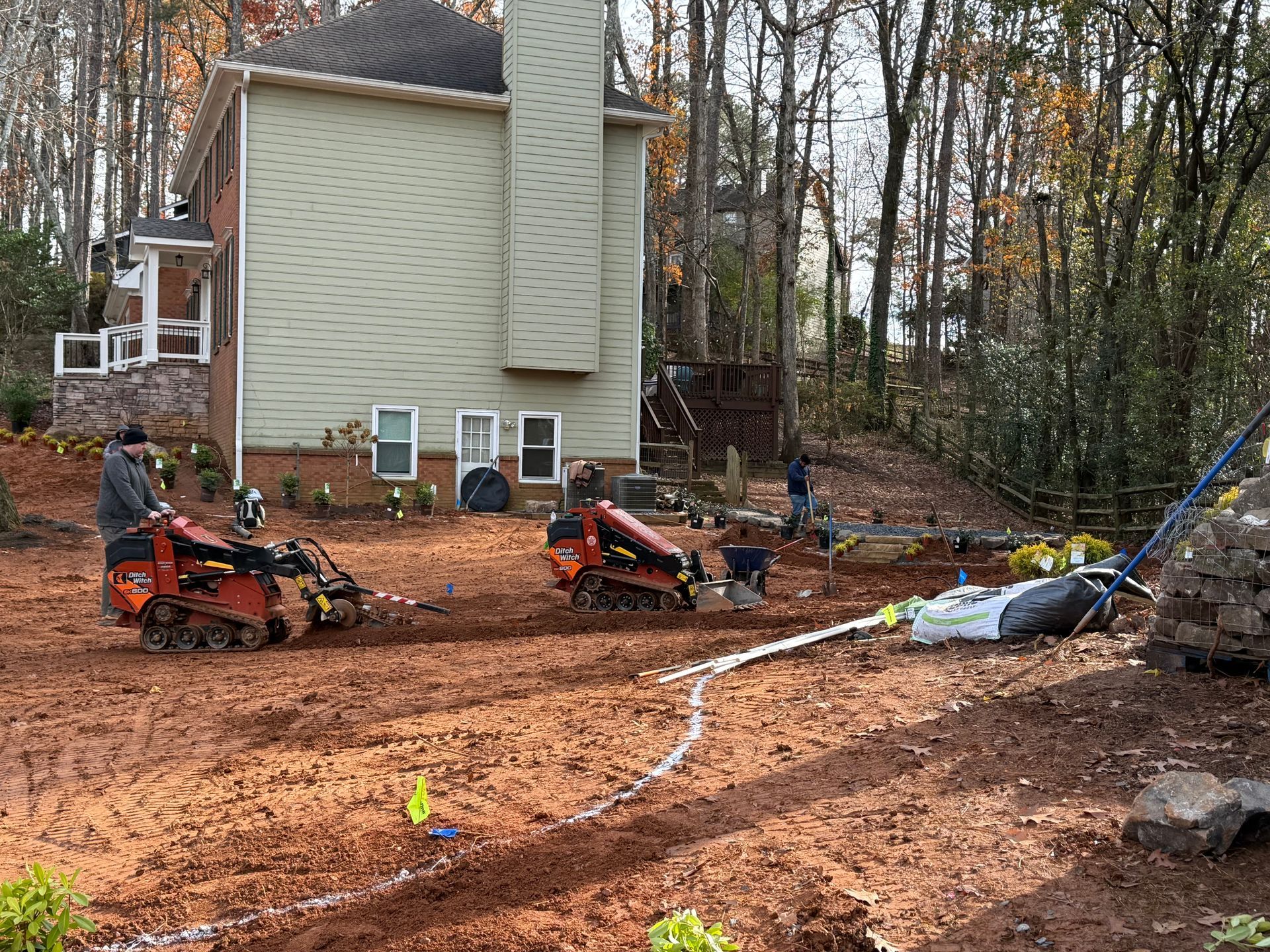 A man is driving a tractor in a dirt field in front of a house.