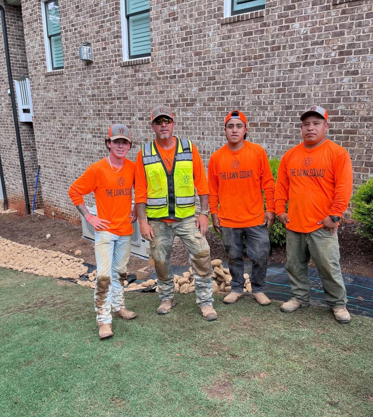 A group of construction workers are posing for a picture in front of a brick building.