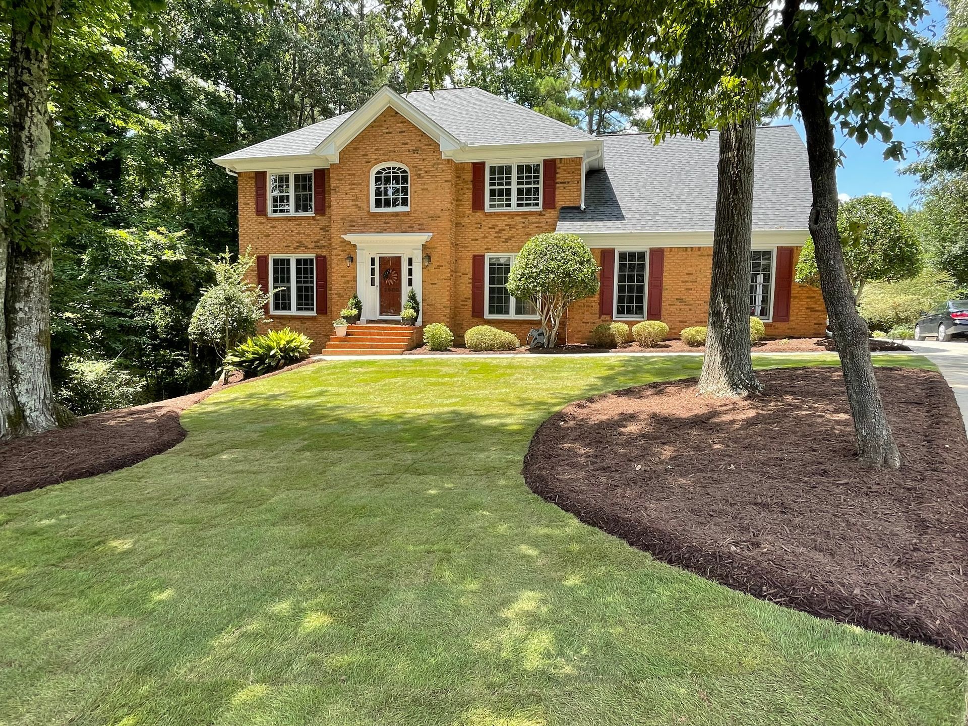 A large brick house with a lush green lawn and trees in front of it.