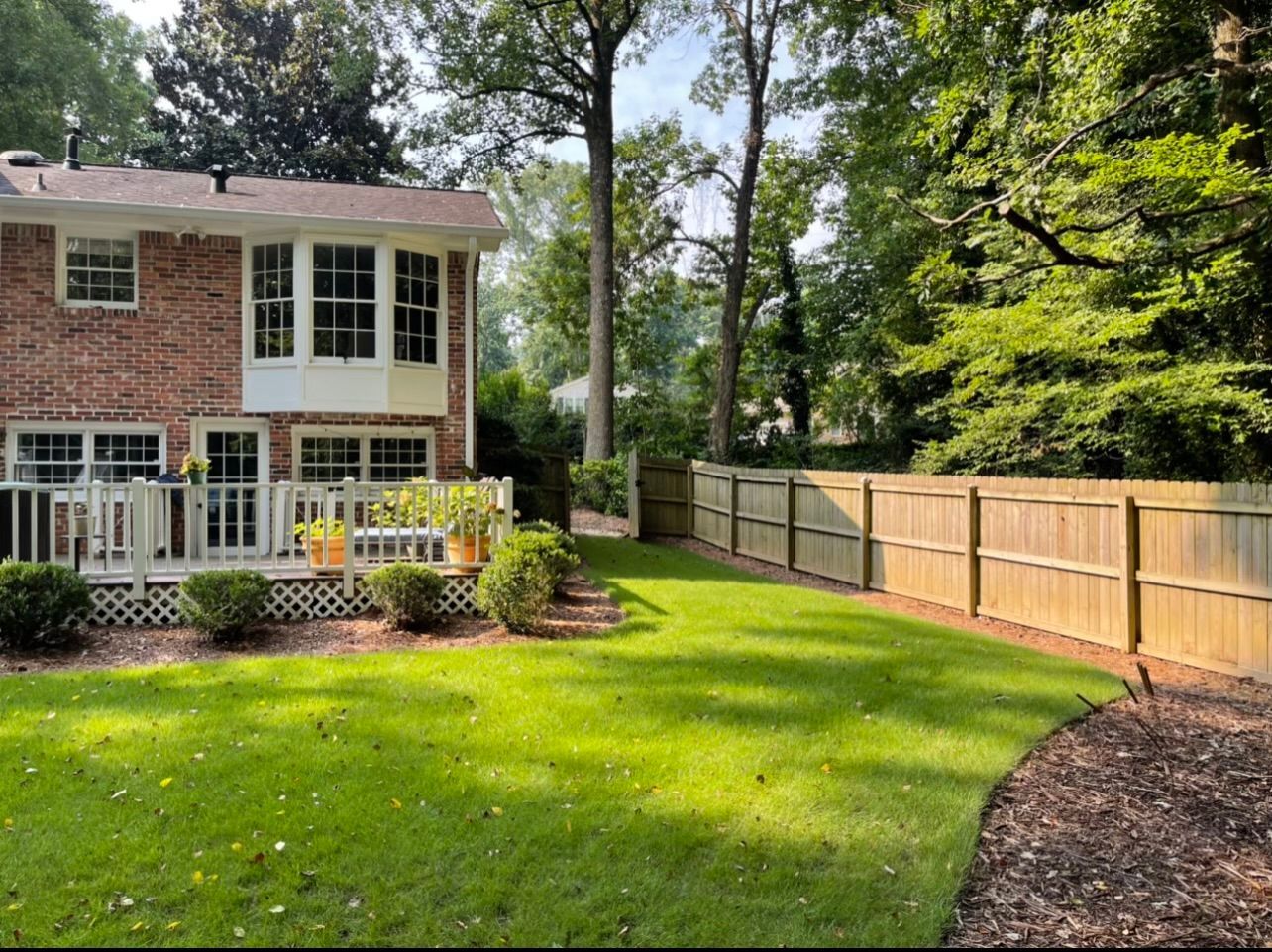 A brick house with a wooden fence and a large lawn in front of it.