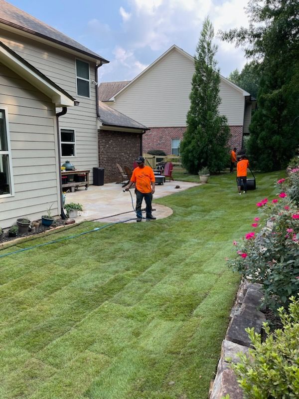 Two men are standing in a lush green lawn in front of a house.