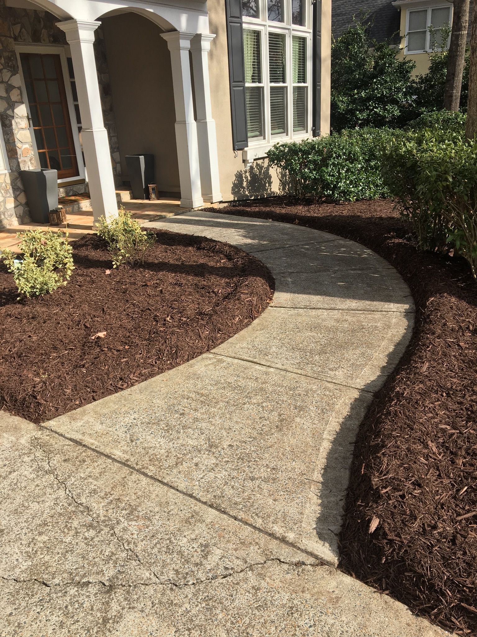 A concrete walkway leading to the front of a house surrounded by mulch.