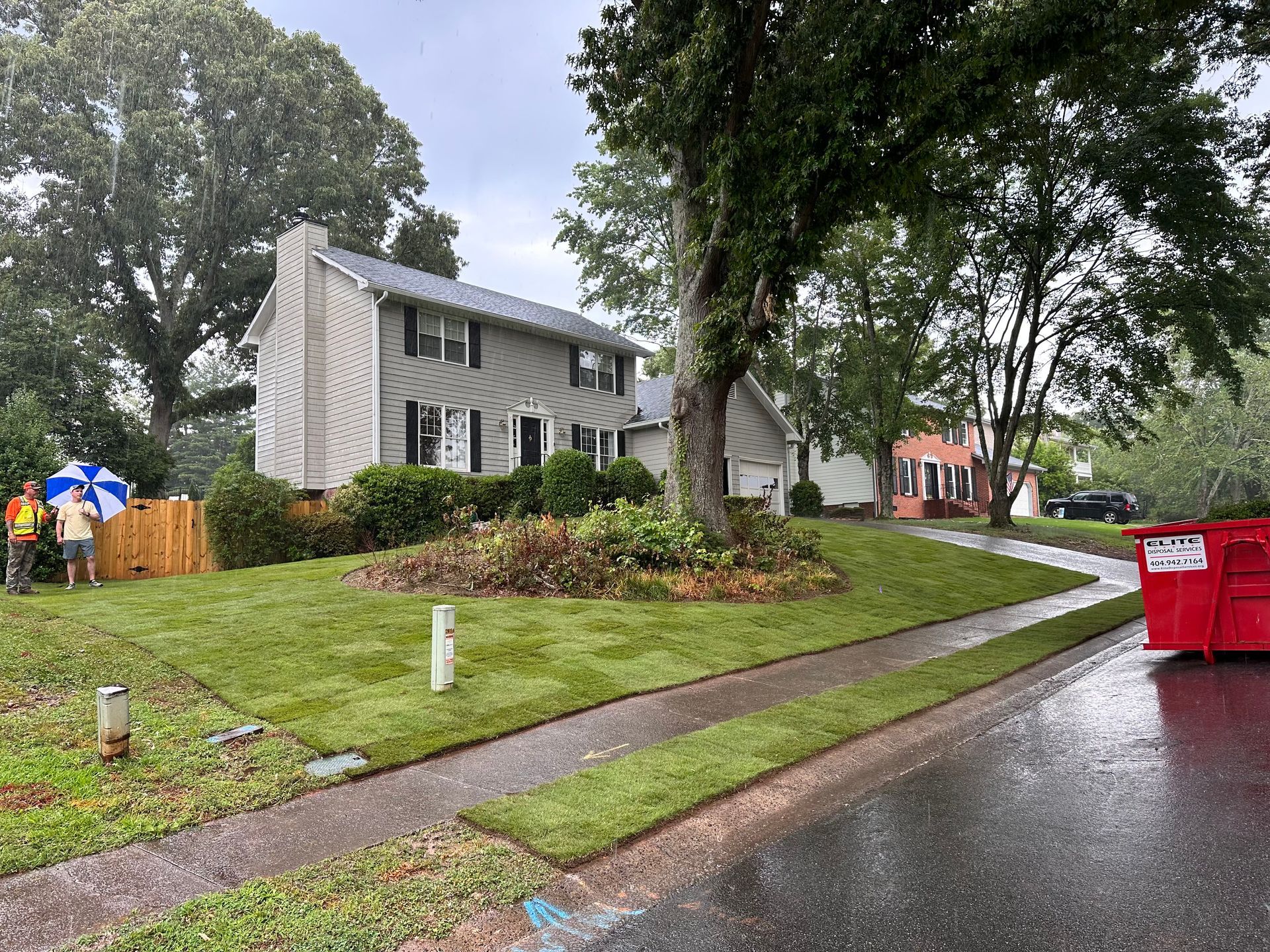 A red dumpster is parked on the side of the road in front of a house.