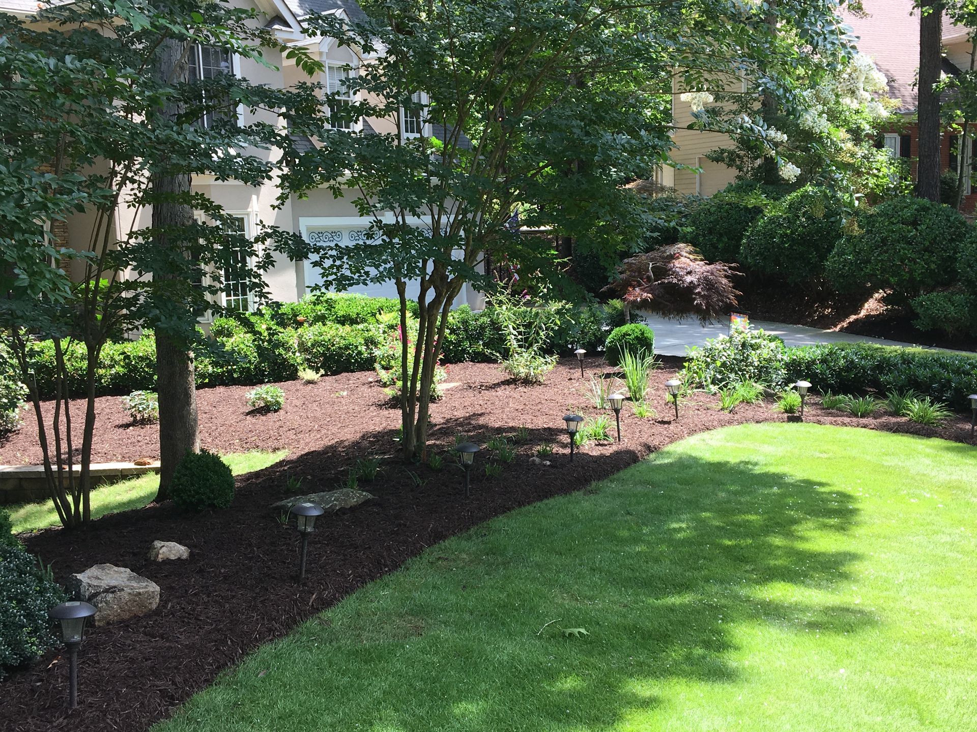 A lush green lawn with trees and mulch in front of a house.