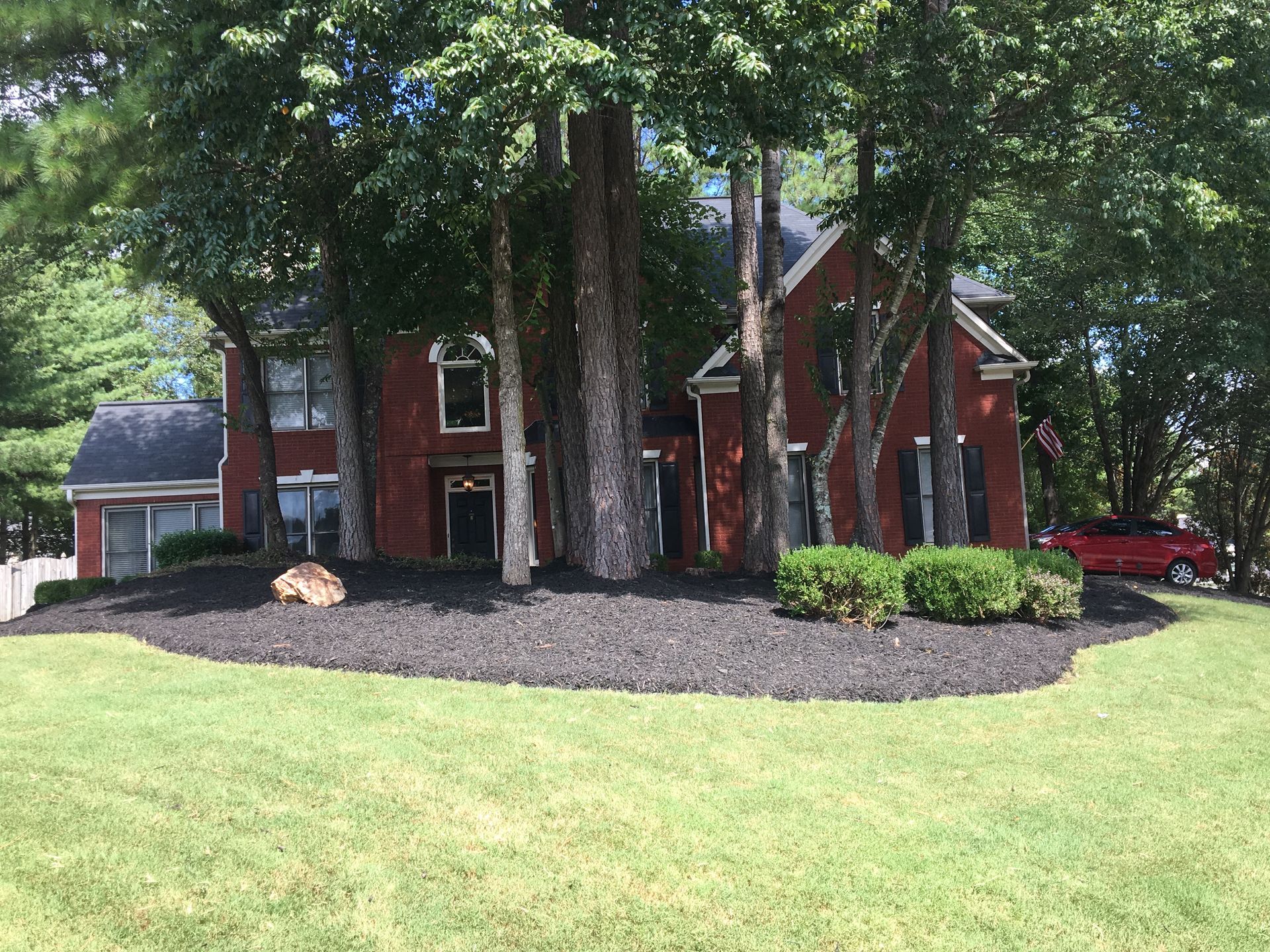 A red brick house with a red truck parked in front of it surrounded by trees.