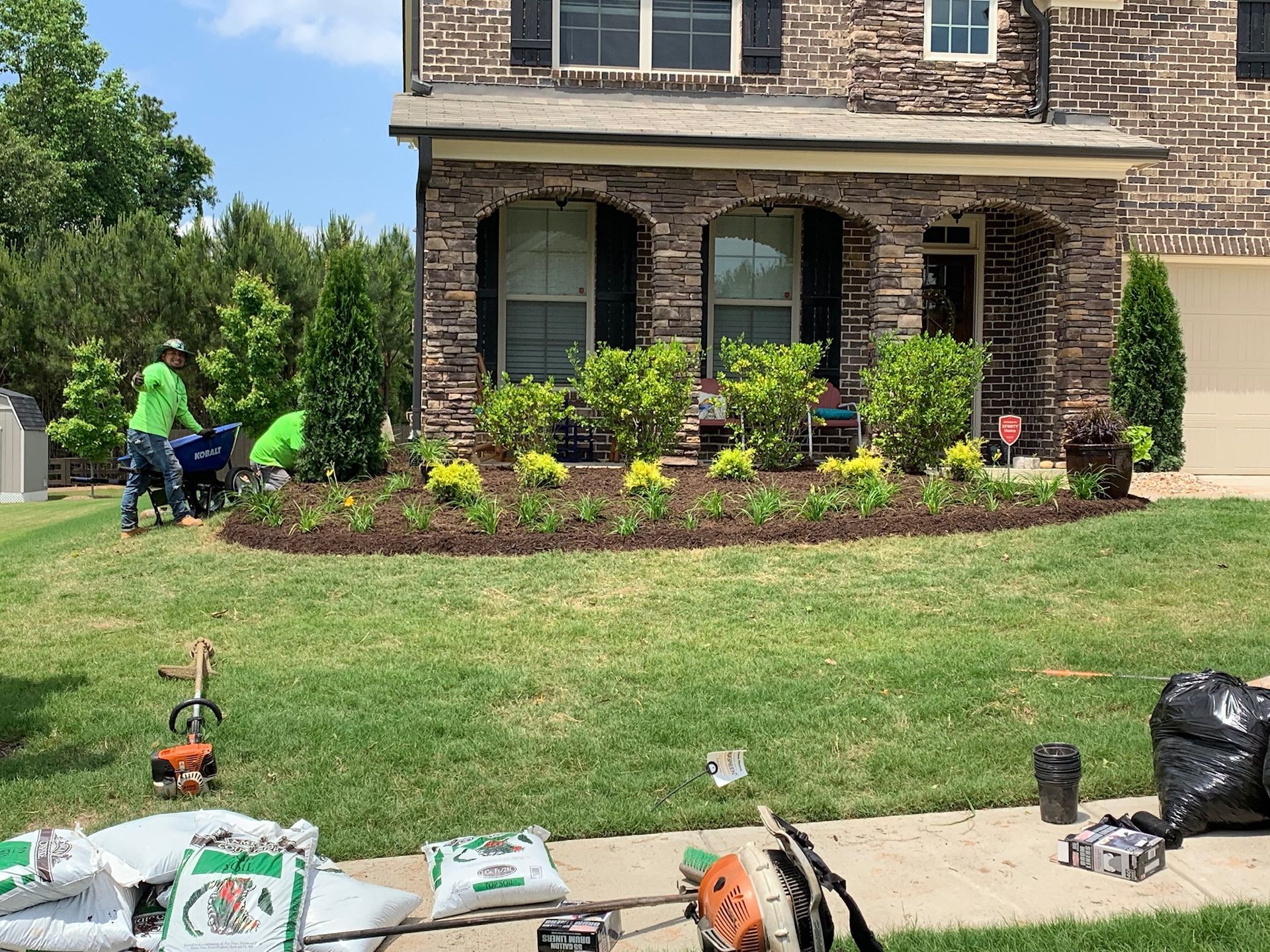 A group of people are working on a lawn in front of a large brick house.