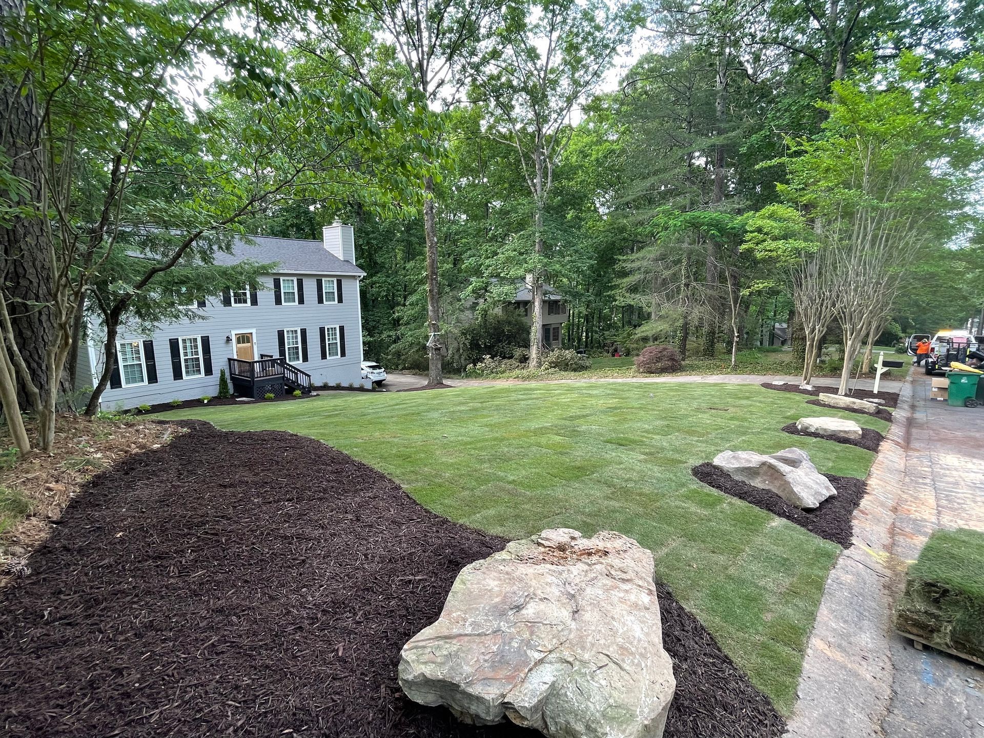 A large white house is sitting on top of a lush green lawn surrounded by trees.
