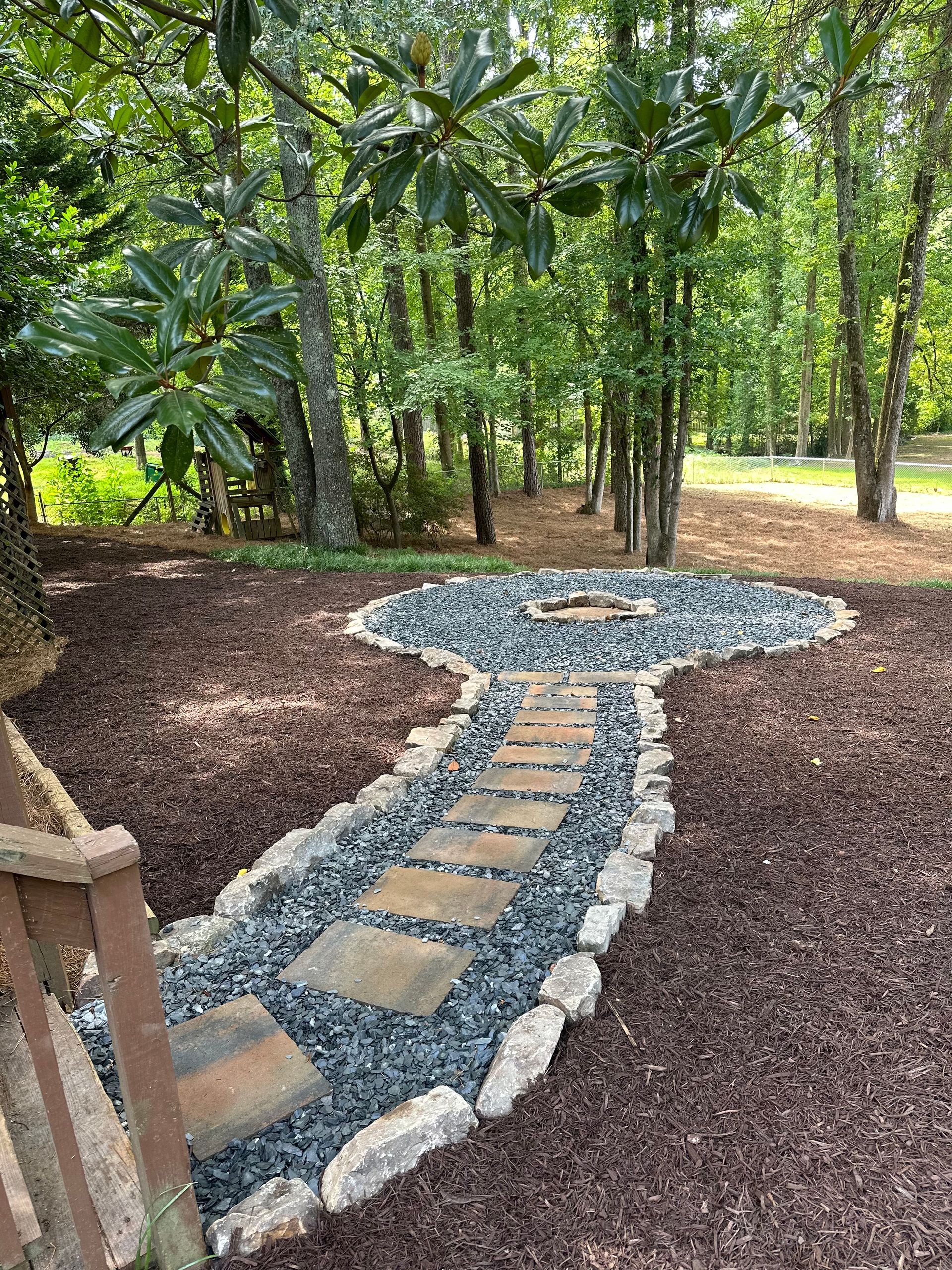 A stone walkway leading to a fire pit in the middle of a forest.