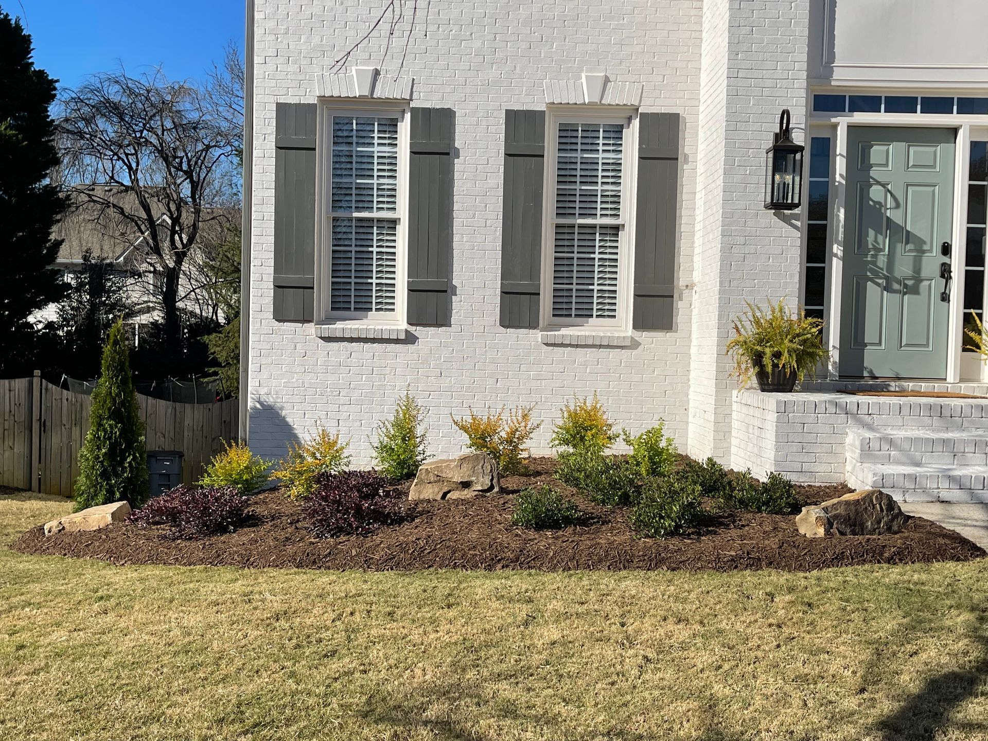 A white brick house with gray shutters and a green door.