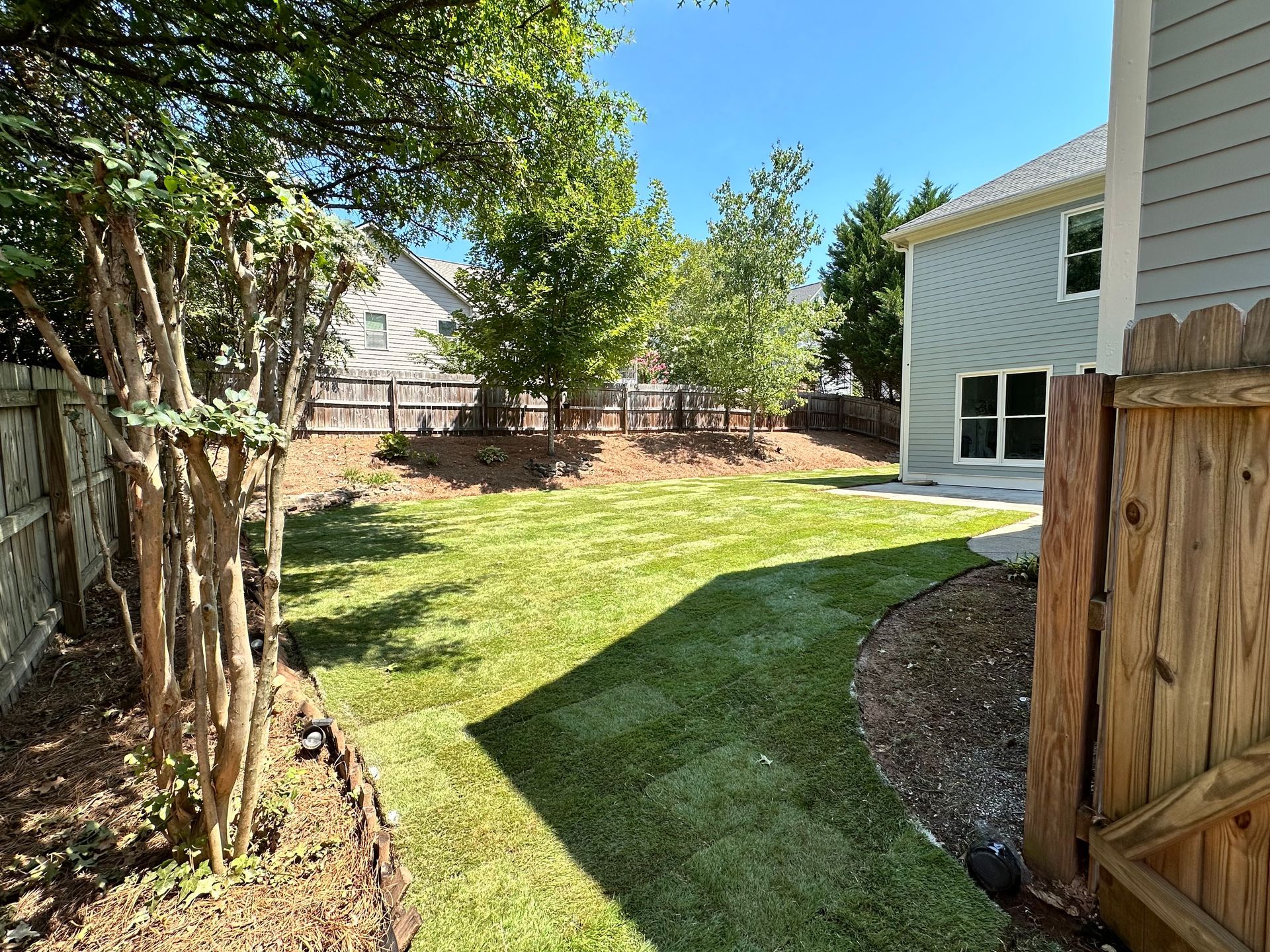 A backyard with a wooden fence and a house in the background.