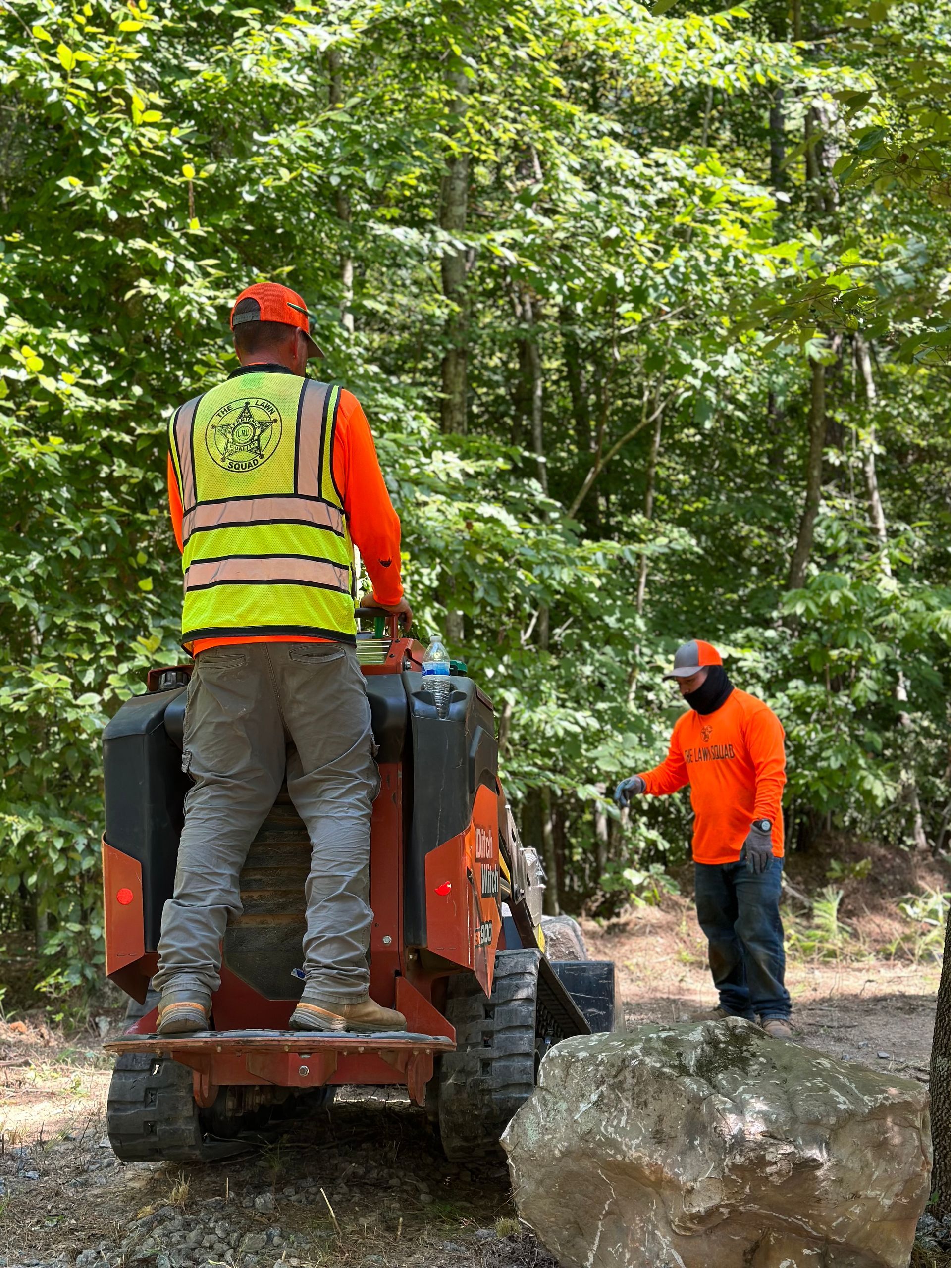Two men are standing next to a tractor in the woods.