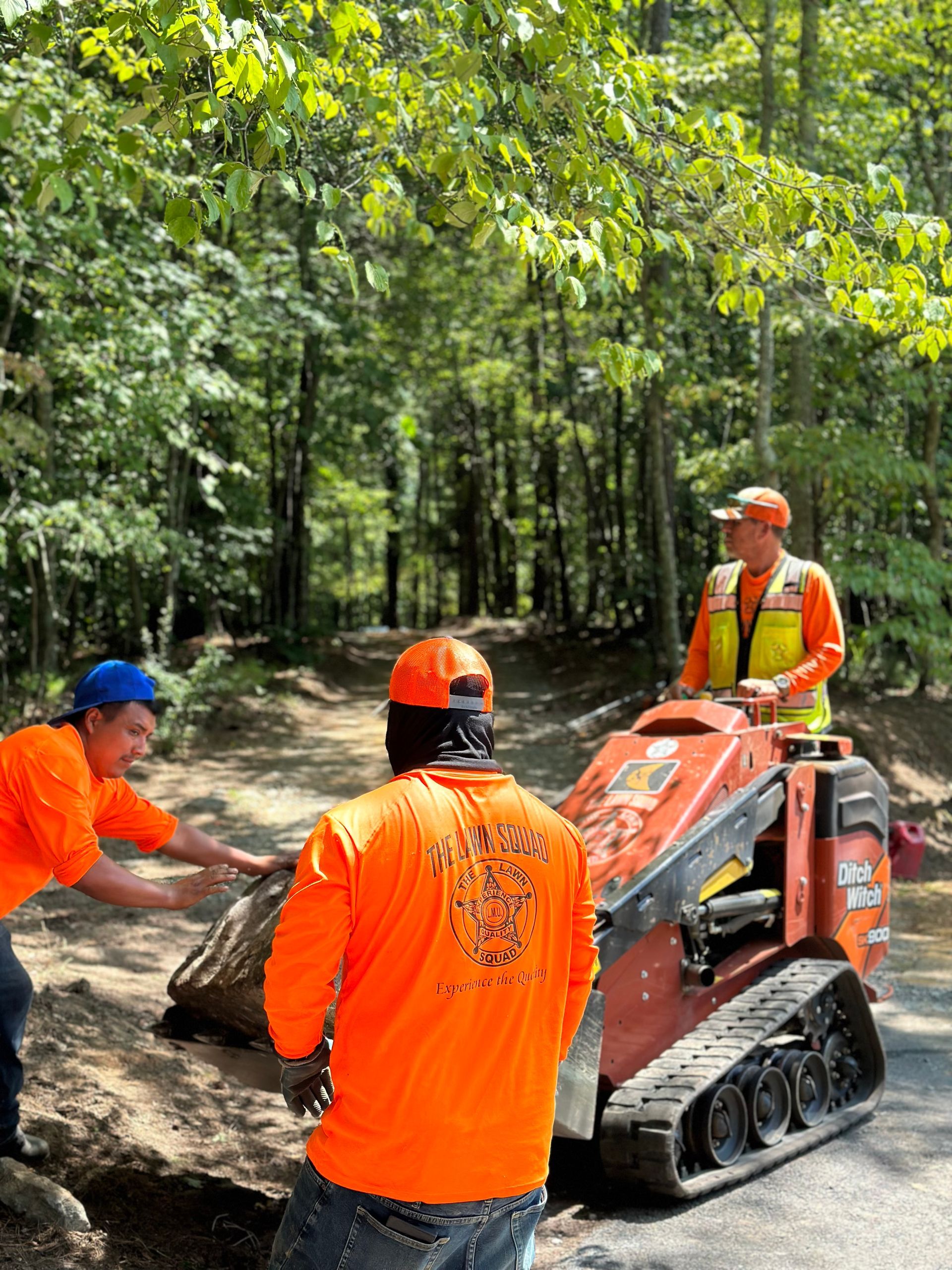 A group of men in orange shirts are working on a machine in the woods.