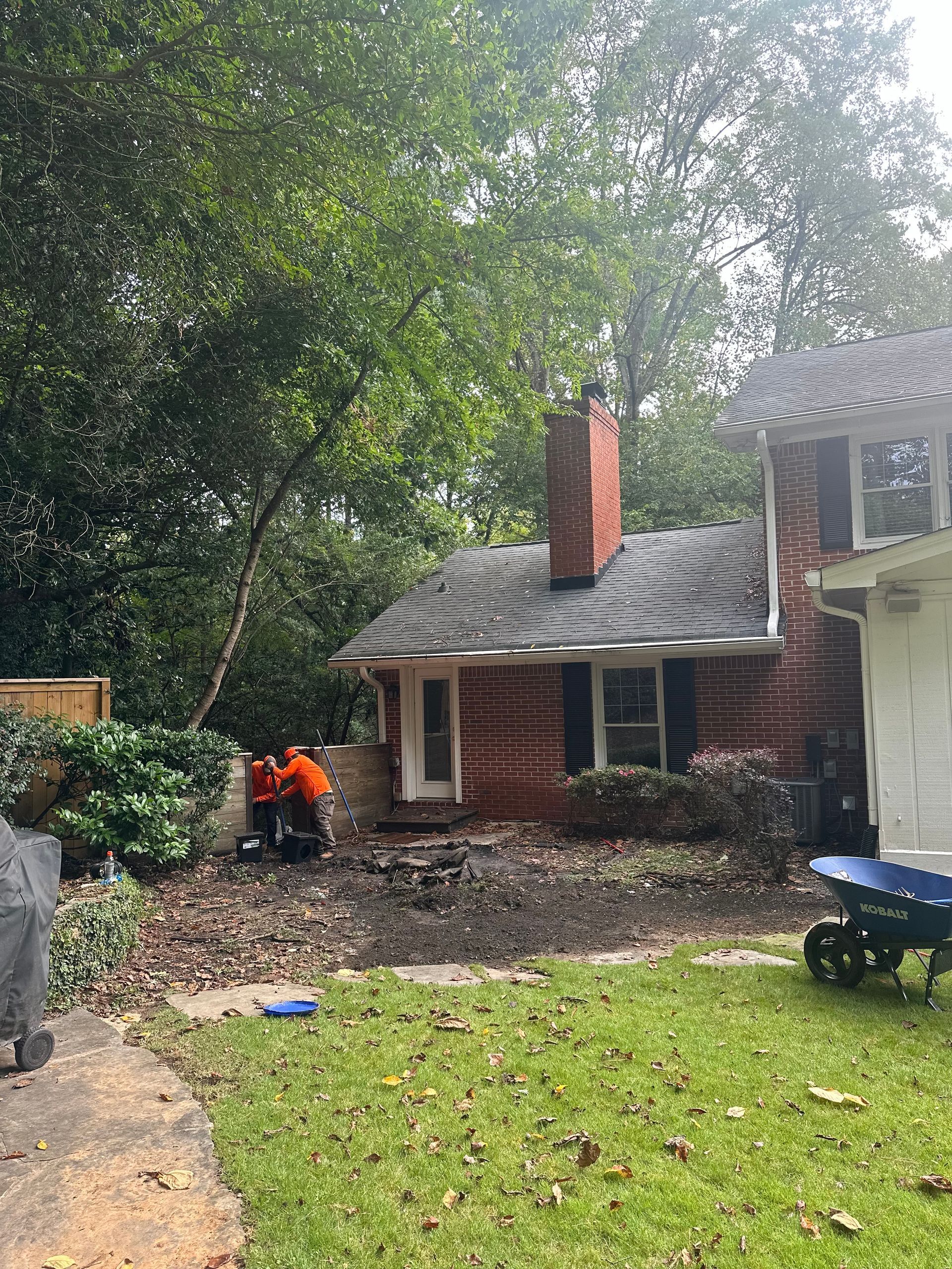 A man is cutting down a tree in front of a brick house.