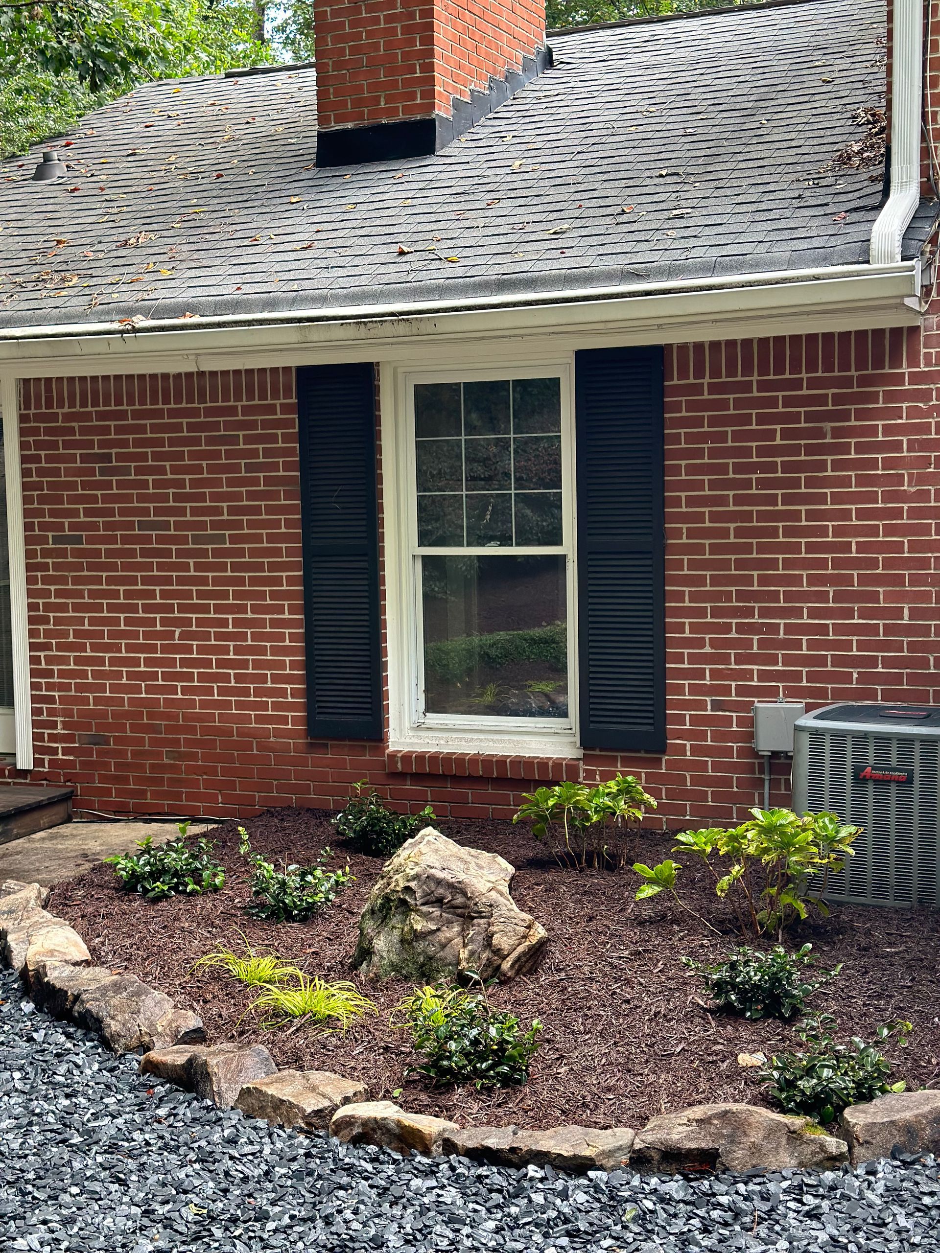 A brick house with black shutters and a garden in front of it.