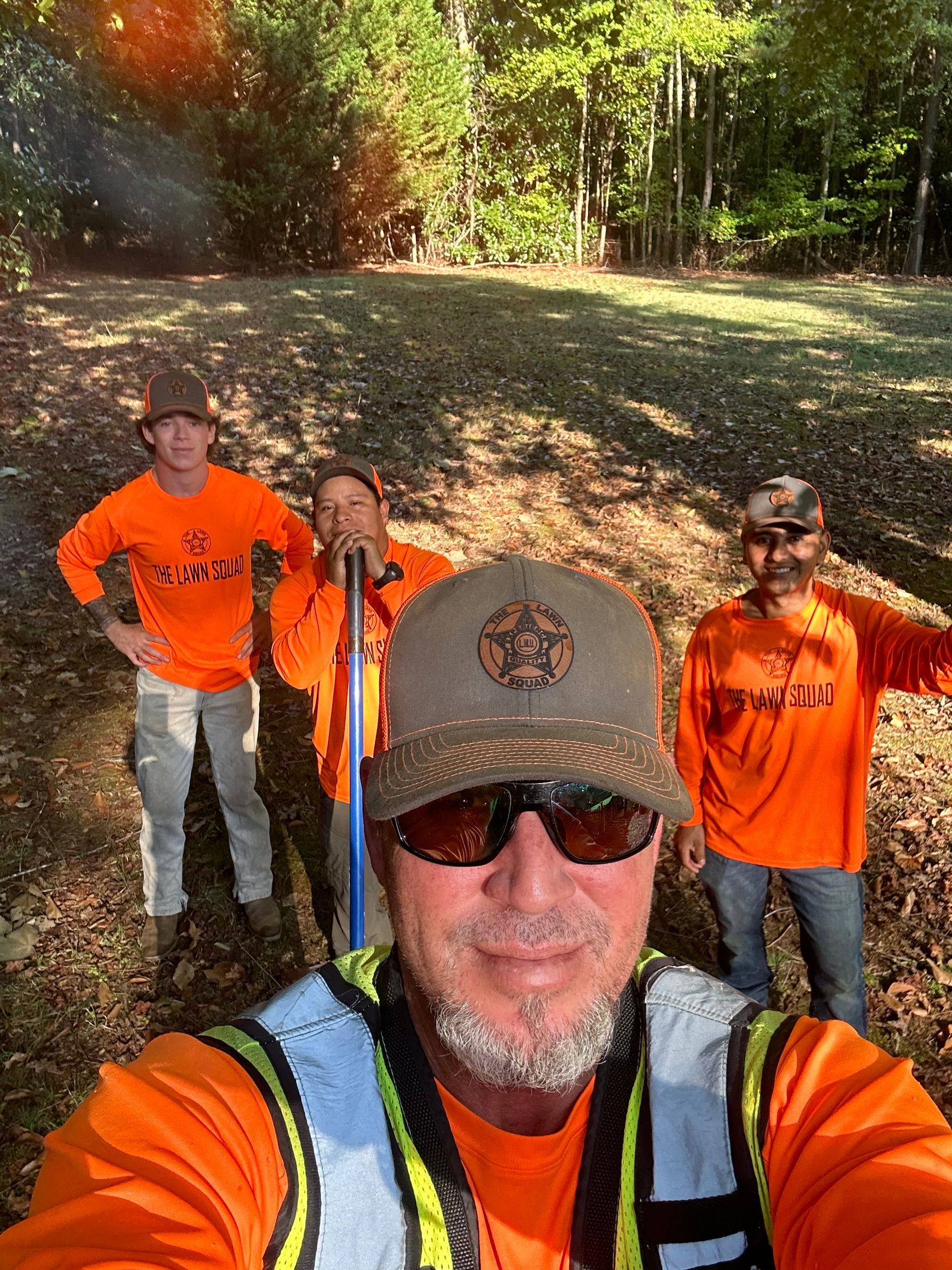 A group of men wearing orange shirts and safety vests are standing in a field.