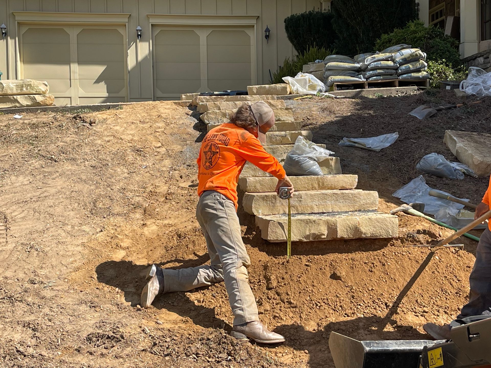 A man in an orange shirt is measuring a stone wall.