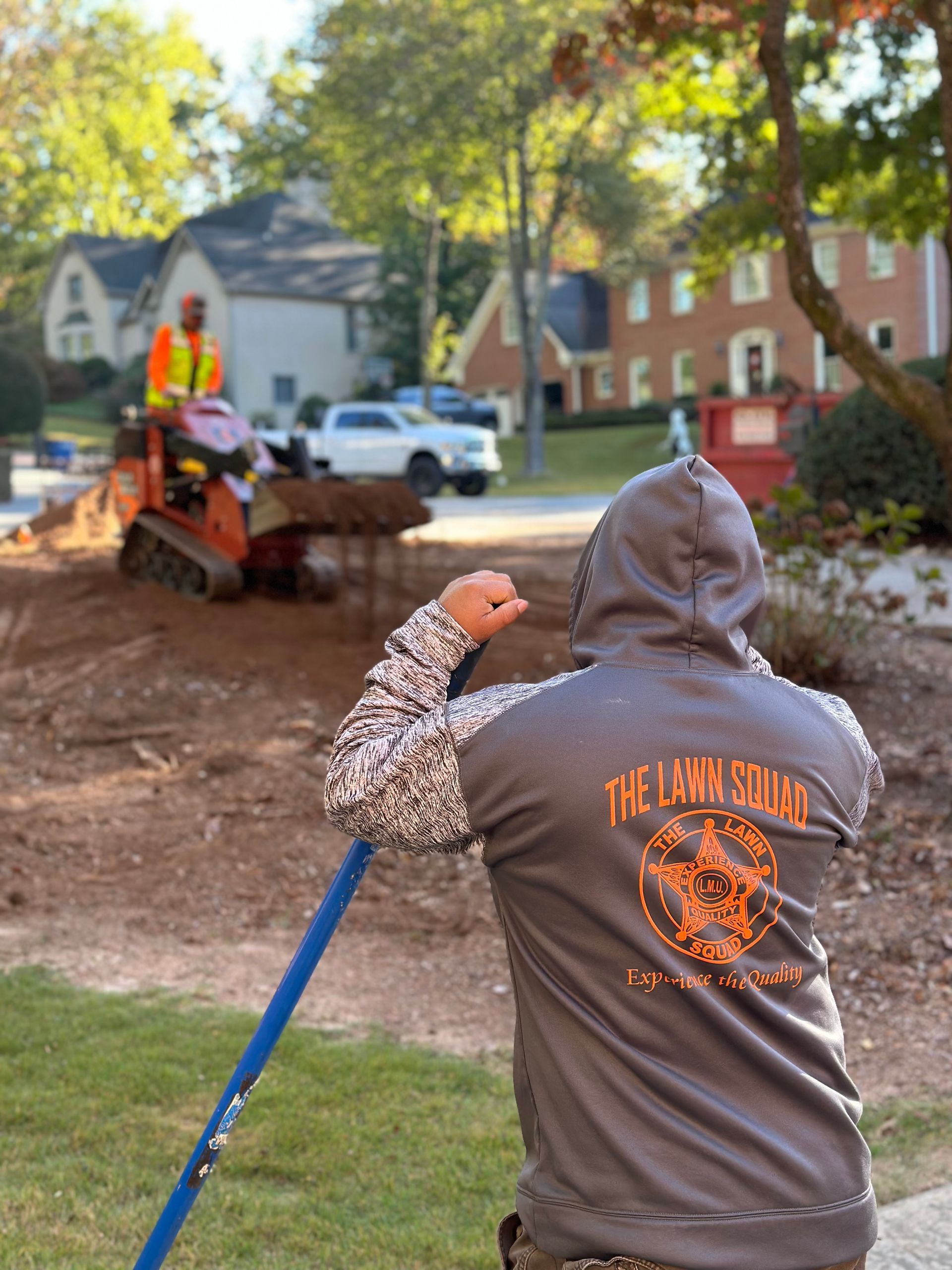 A man in a hoodie is holding a shovel in front of a bulldozer.