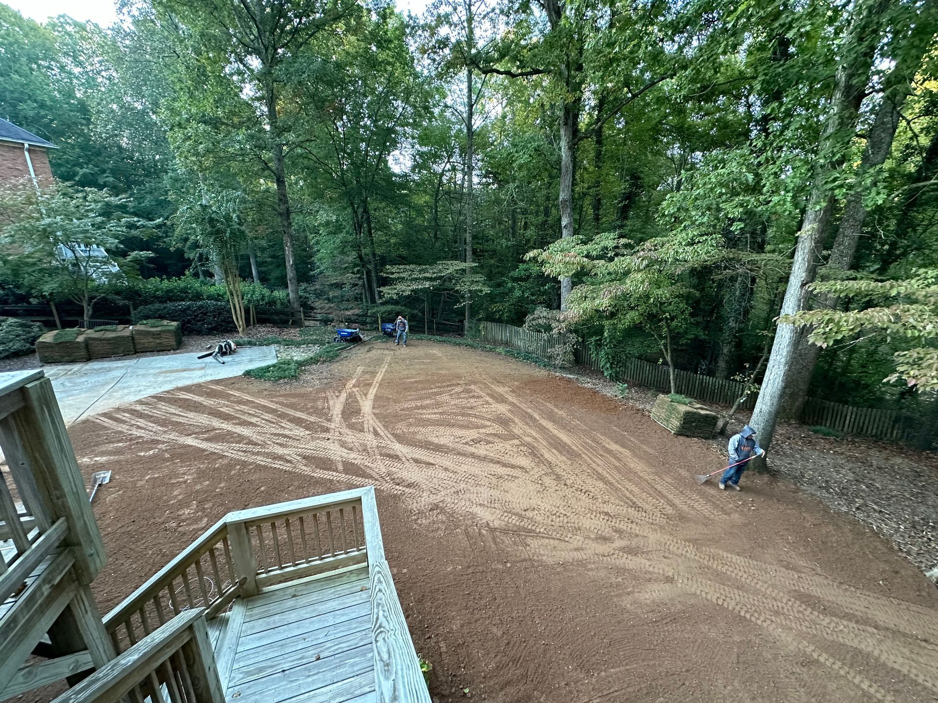 A man is standing in a dirt field next to a wooden deck.