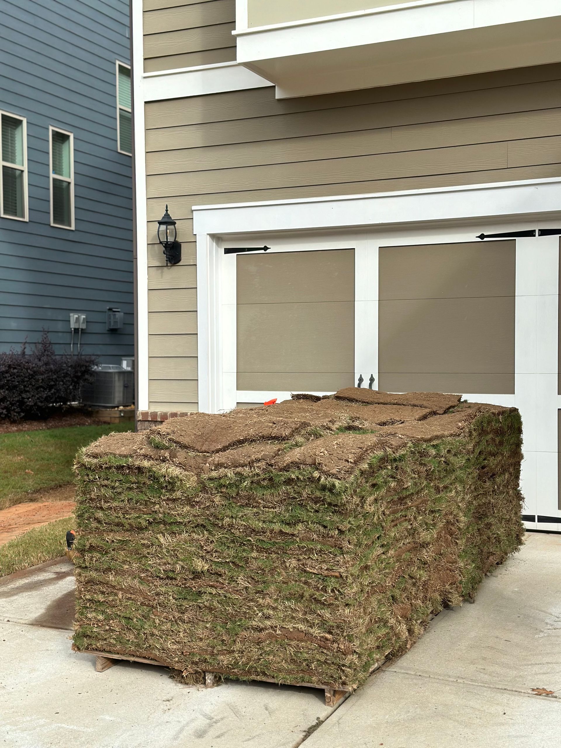 A large stack of grass is sitting in front of a house
