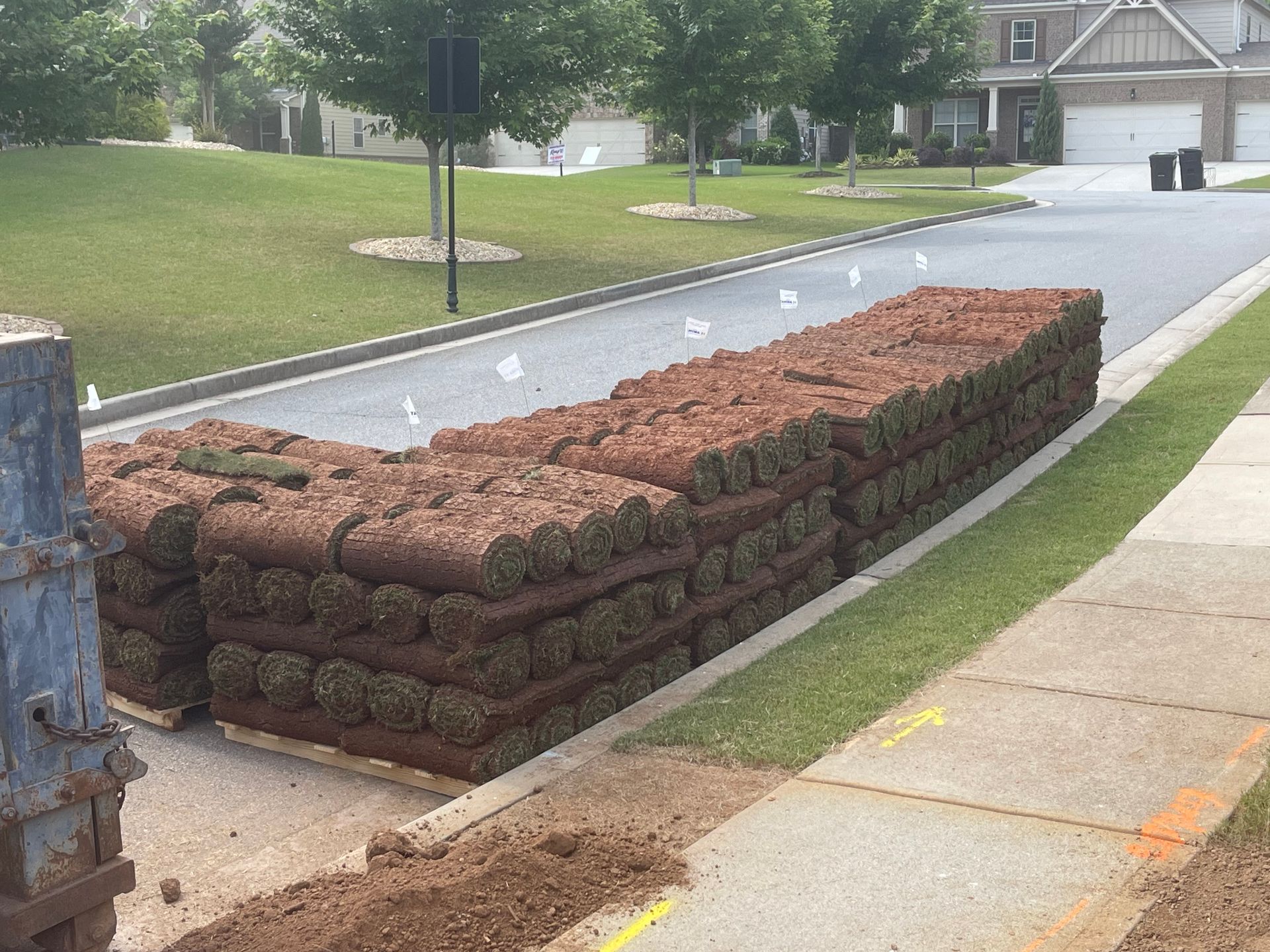 A stack of rolls of grass is sitting on the sidewalk in front of a house.