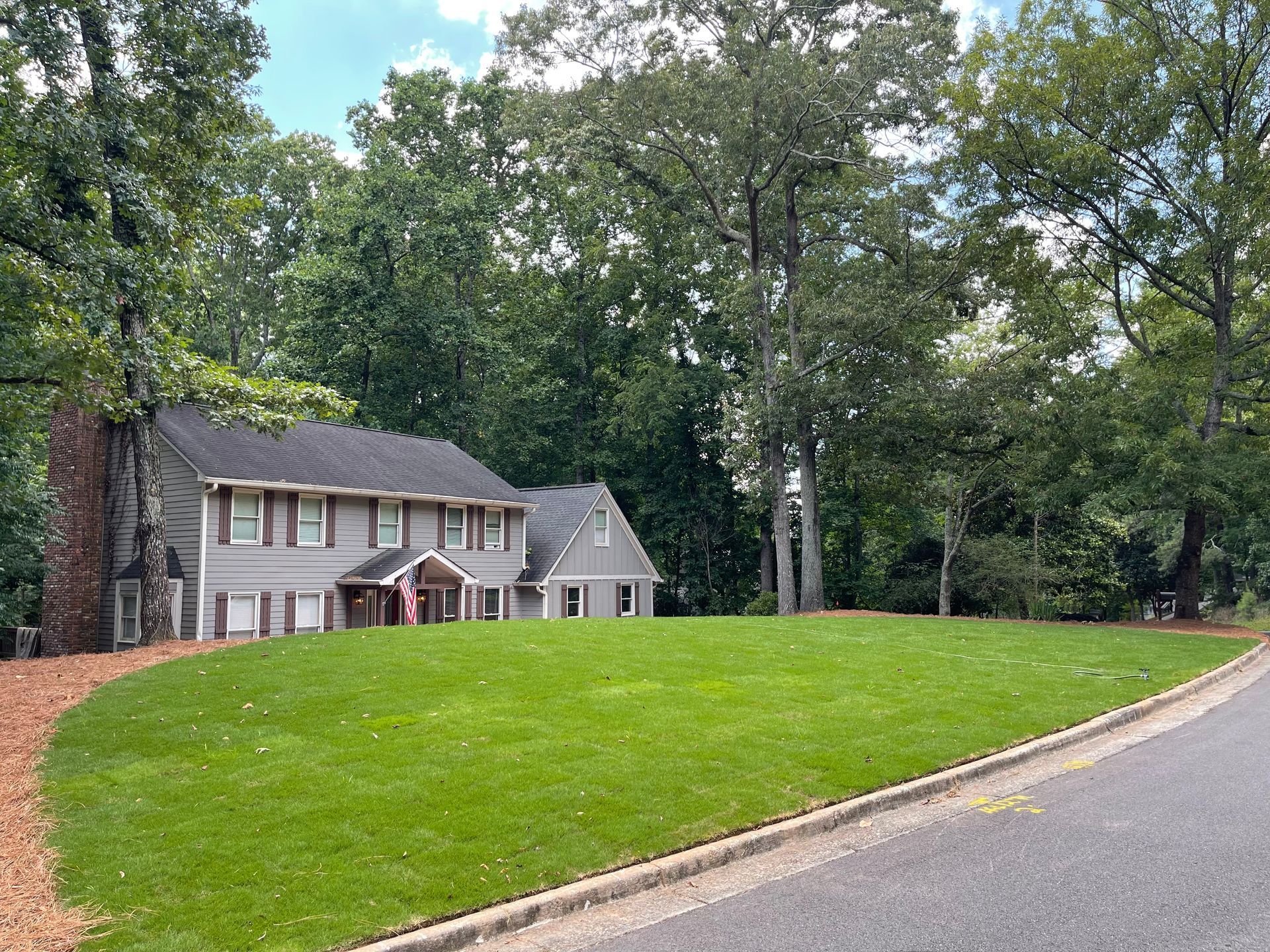 A large house with a large lawn in front of it is surrounded by trees.