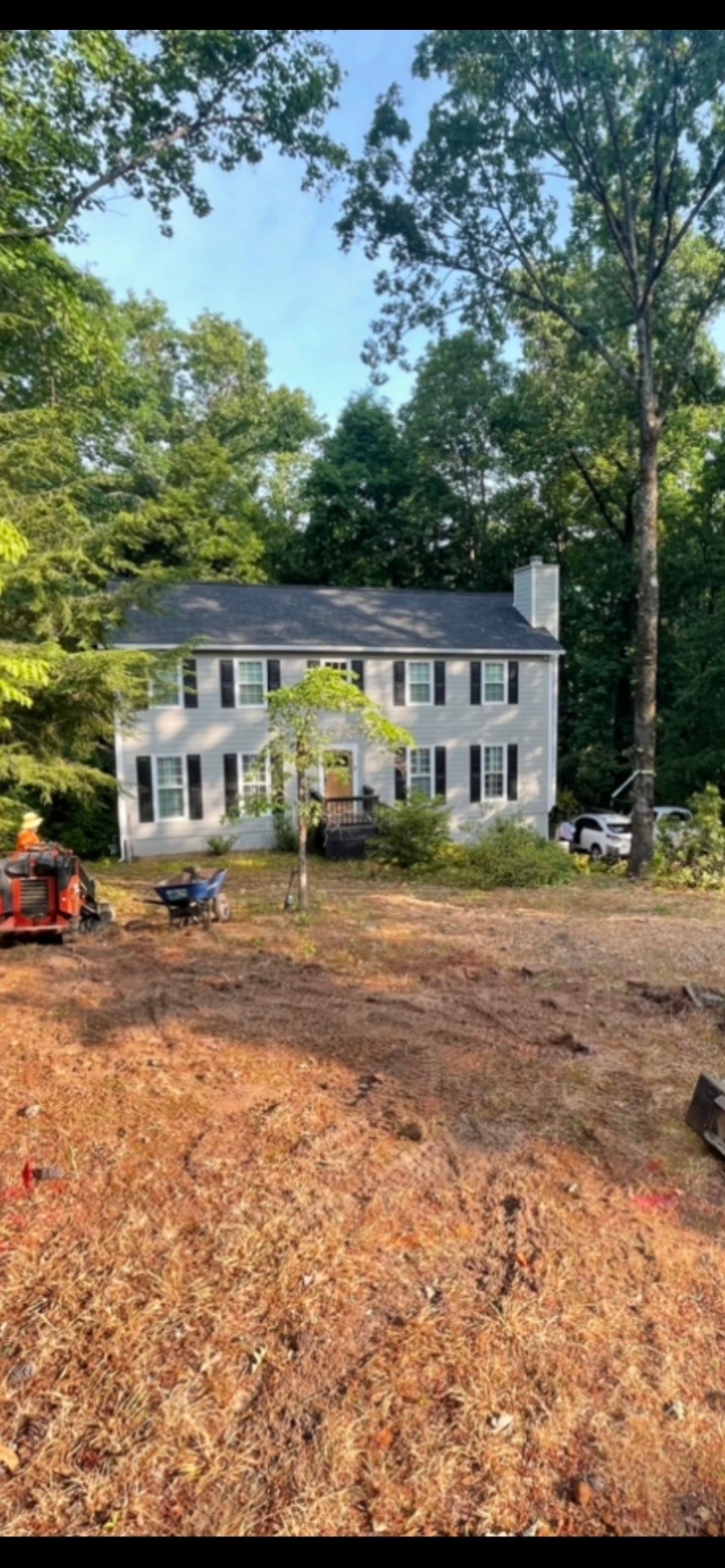 A large white house is sitting in the middle of a dirt field surrounded by trees.