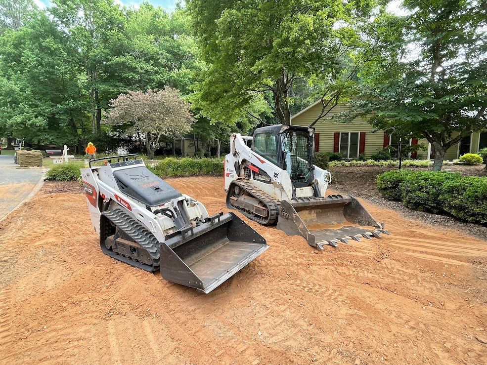 Two bulldozers are sitting on top of a dirt field in front of a house.