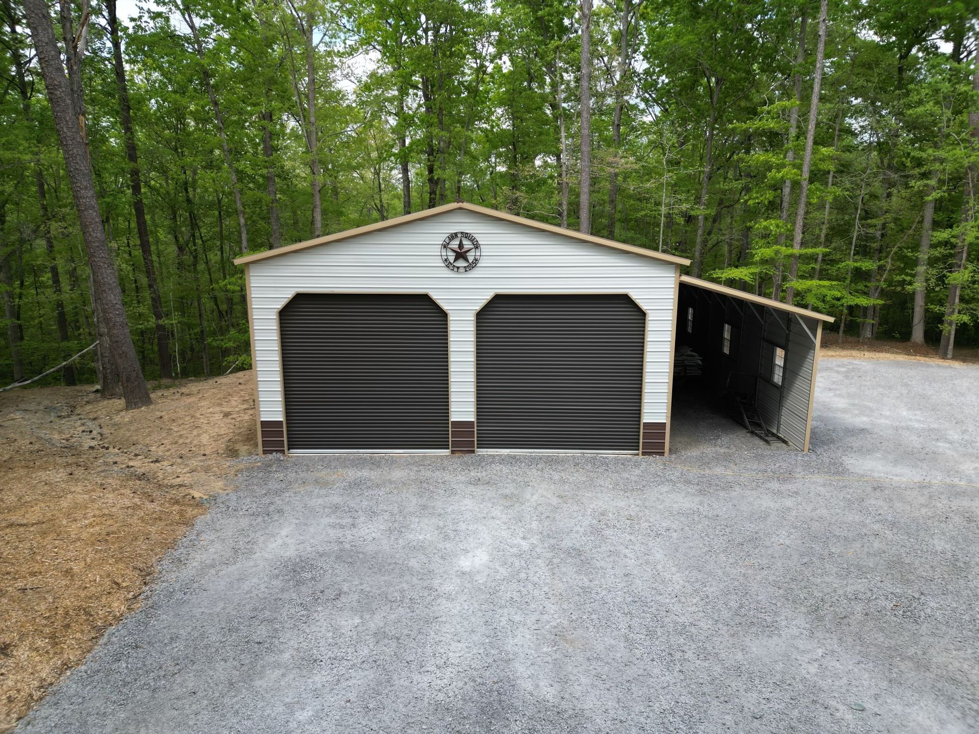 A white garage with black doors is sitting on top of a gravel driveway.