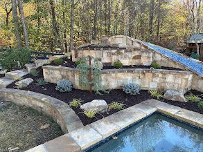 A swimming pool surrounded by a stone wall and trees in a backyard.