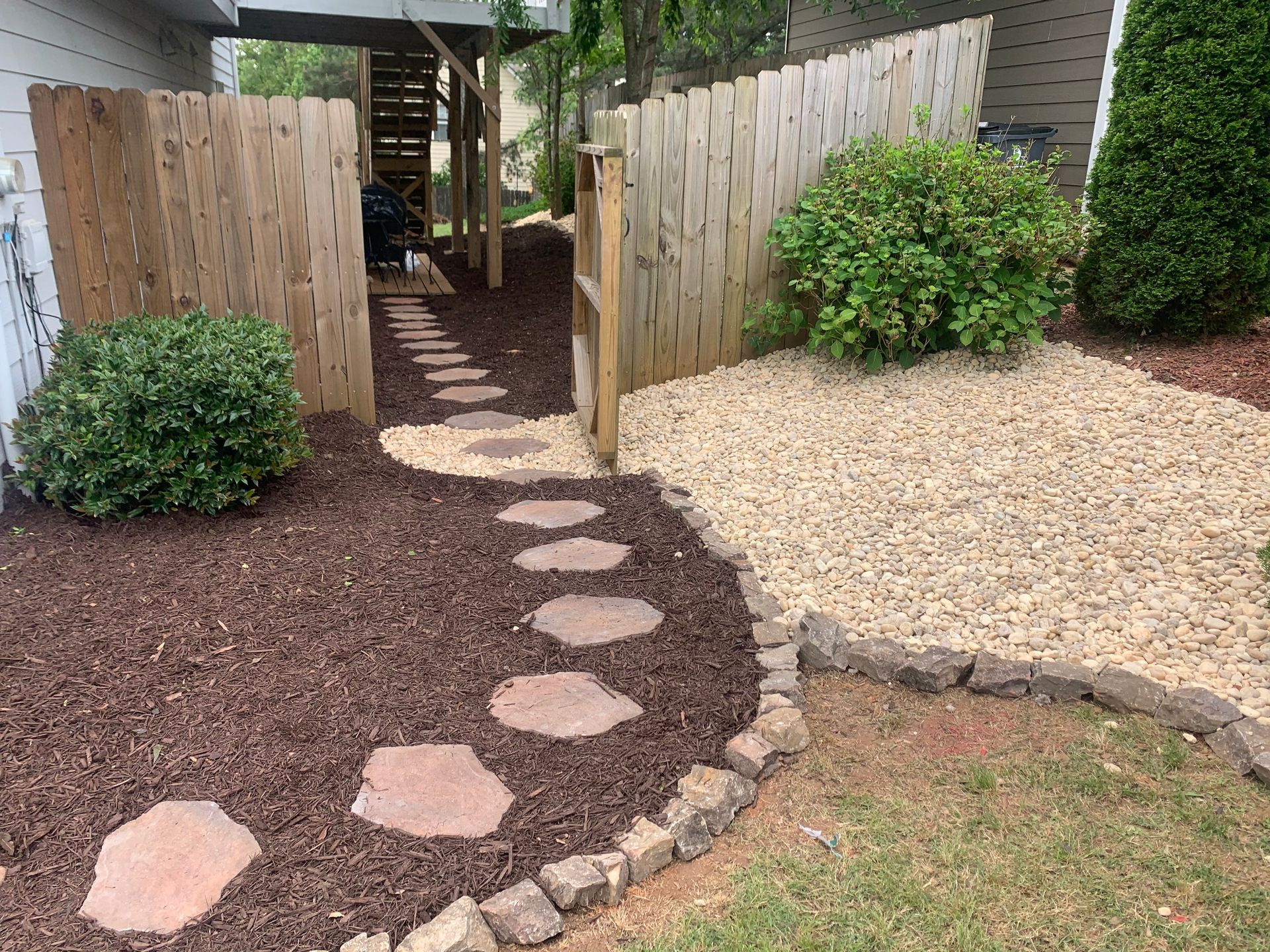 A stone walkway leading to a wooden fence in a backyard.