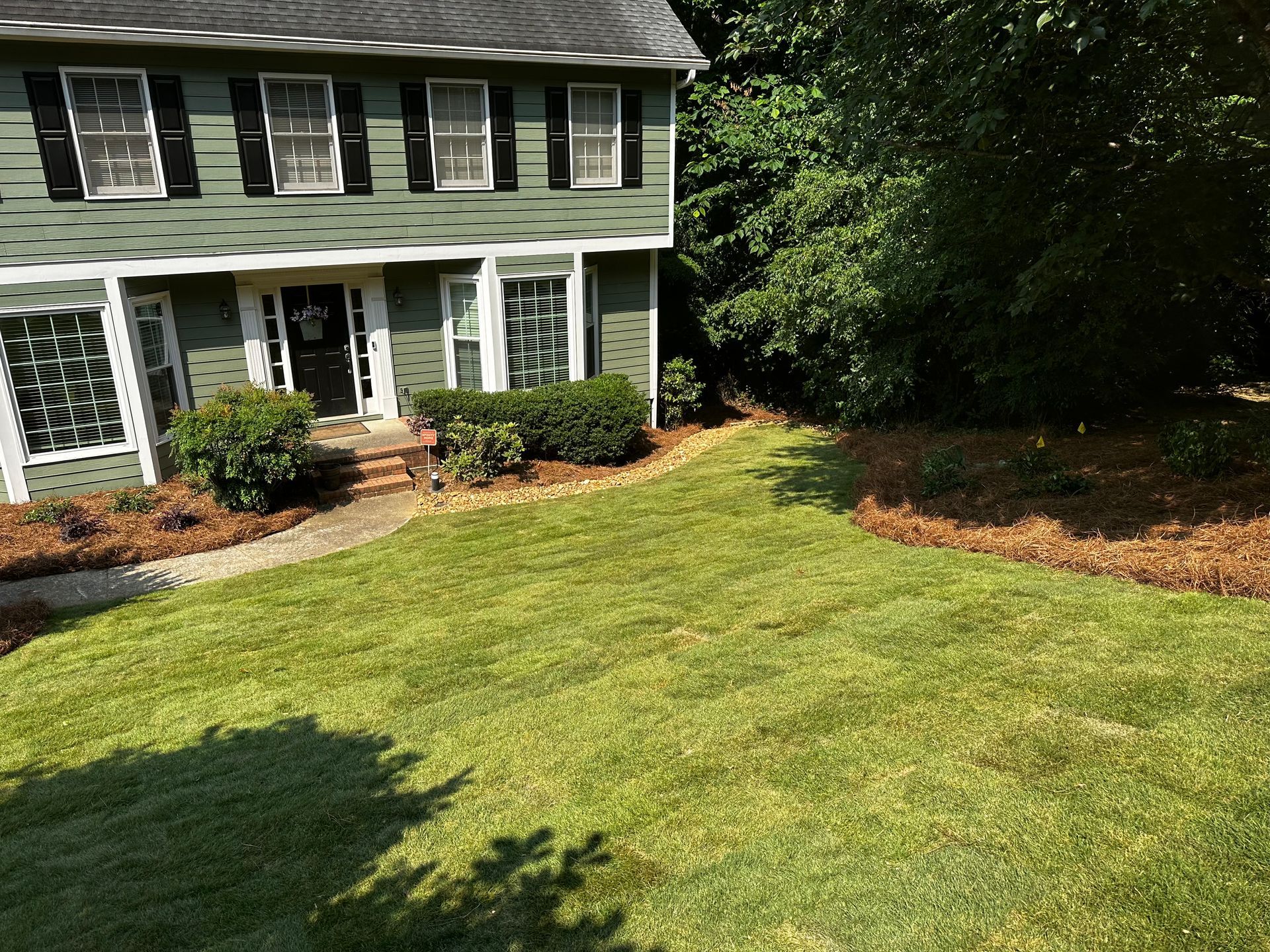 A green house with a lush green lawn in front of it.