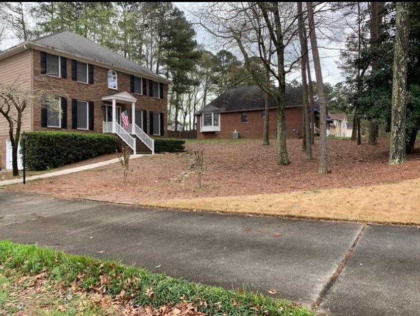 A large brick house is surrounded by trees and a driveway.