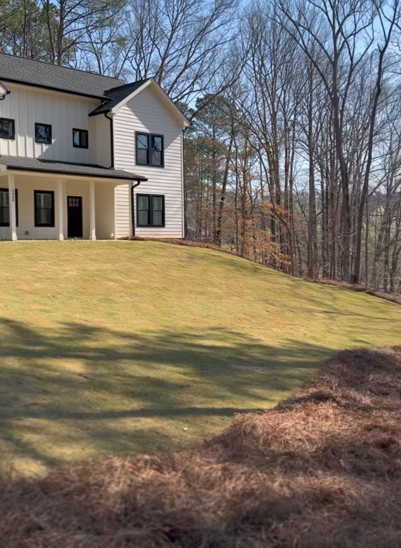 A large white house is sitting on top of a lush green hill surrounded by trees.