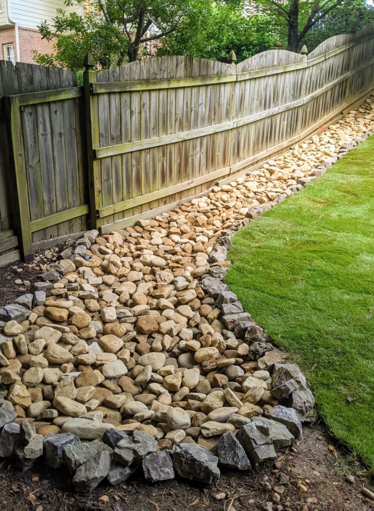 A wooden fence is surrounded by rocks in a backyard.