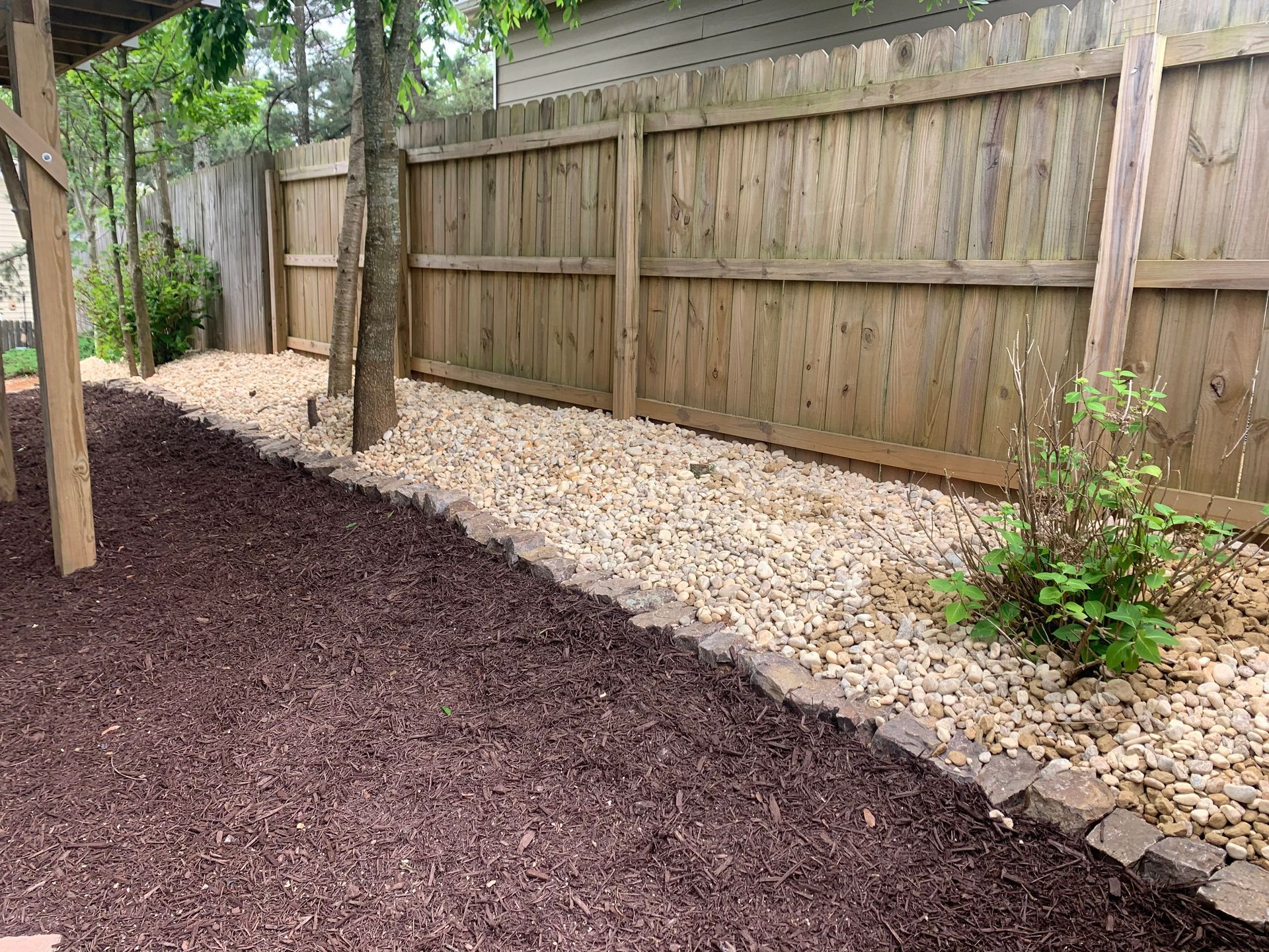 A wooden fence surrounds a gravel path in a backyard.