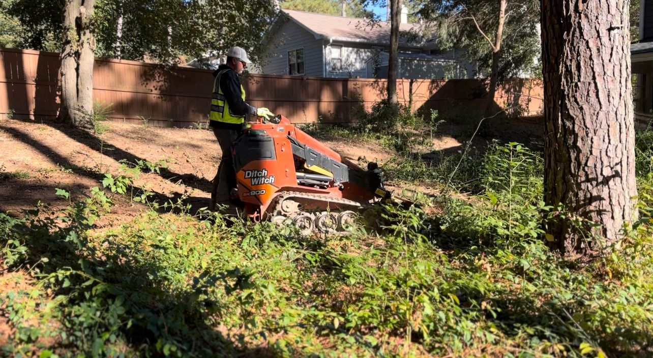 A man is using a machine to stump a tree in a yard.