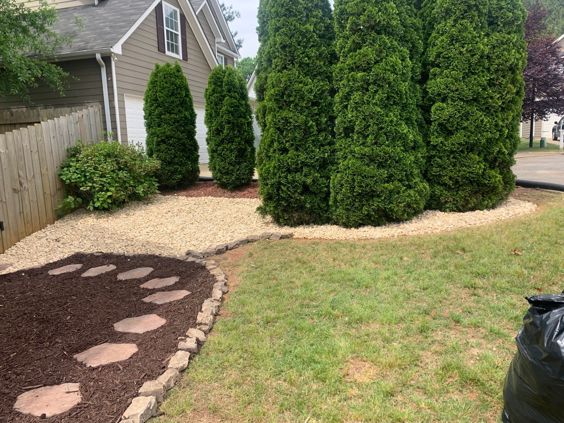 A lush green yard with trees and rocks in front of a house.