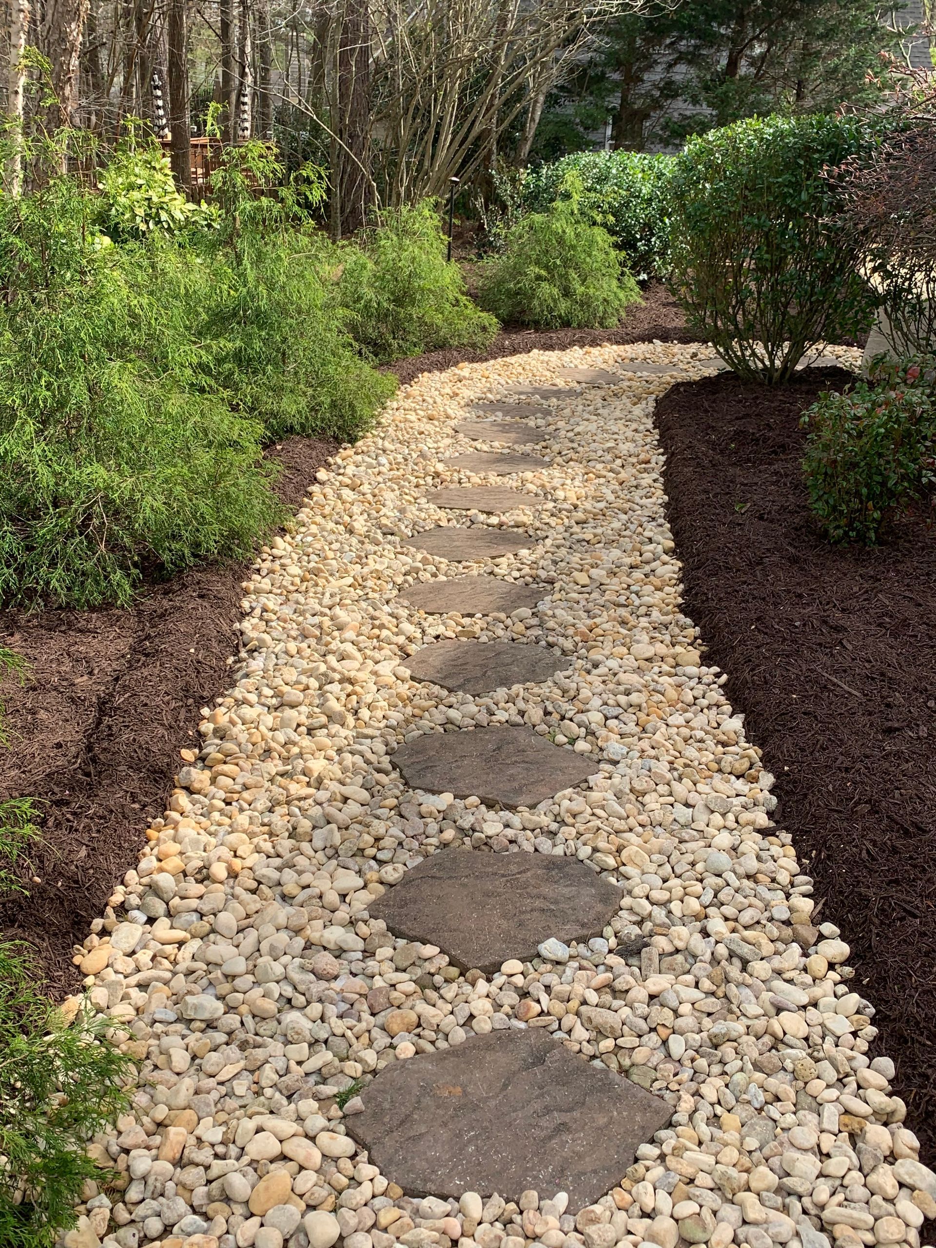 A stone walkway in a garden surrounded by trees and bushes.