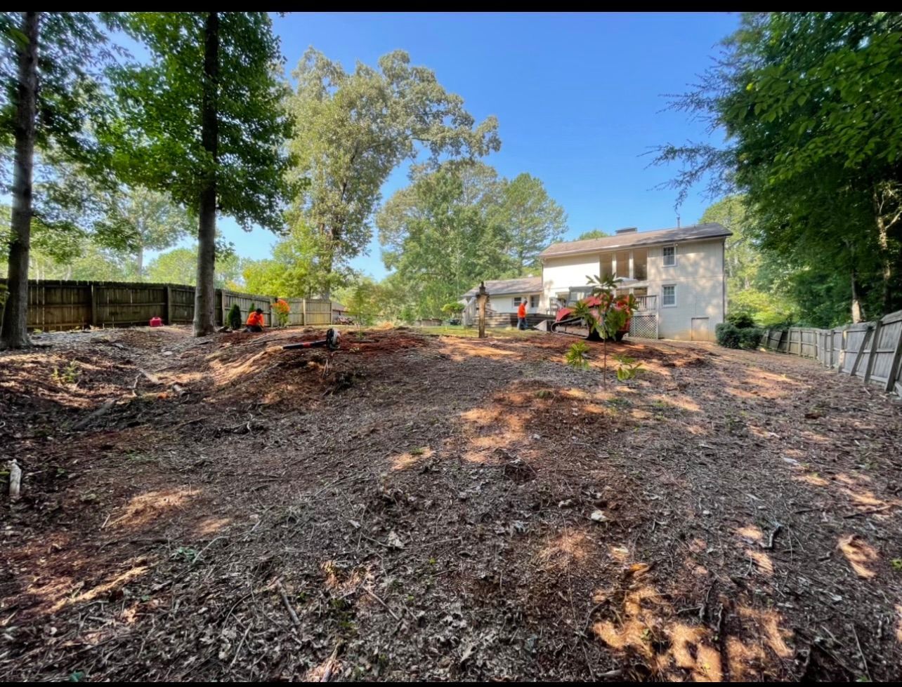 A large pile of dirt in front of a house with trees in the background.