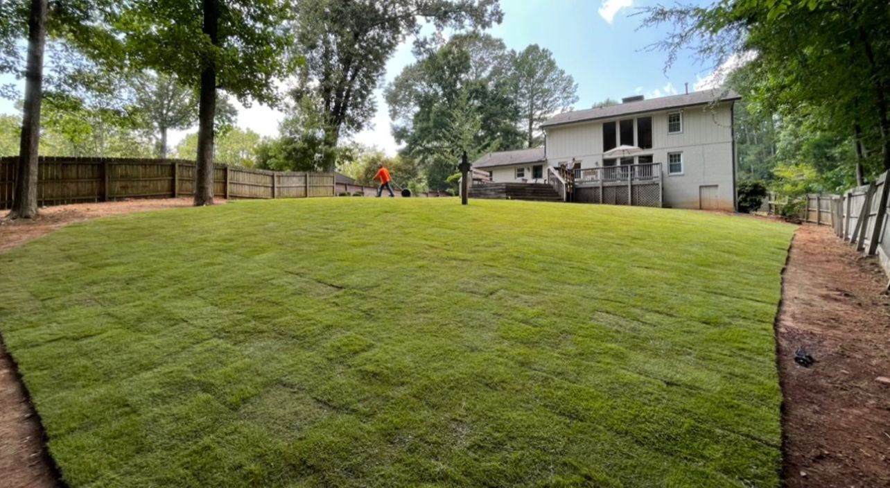 A large lawn with a fence and a house in the background.