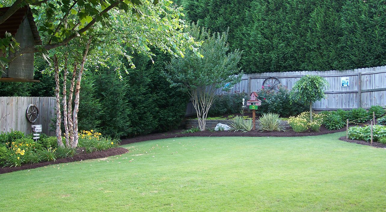 A large lush green lawn with a wooden fence in the background.