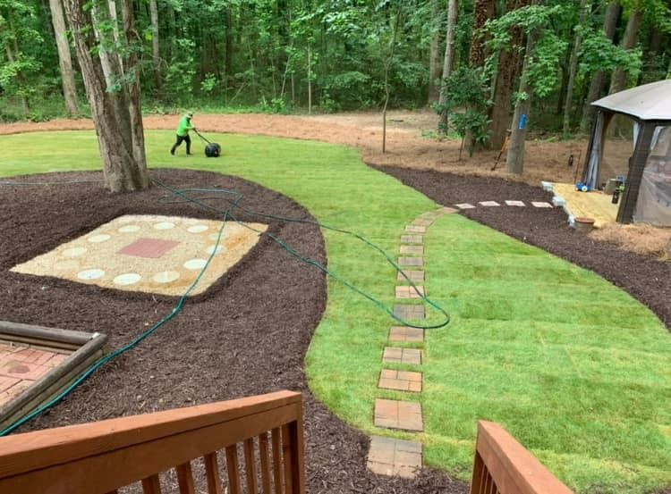 A man is mowing a lush green lawn in a backyard.