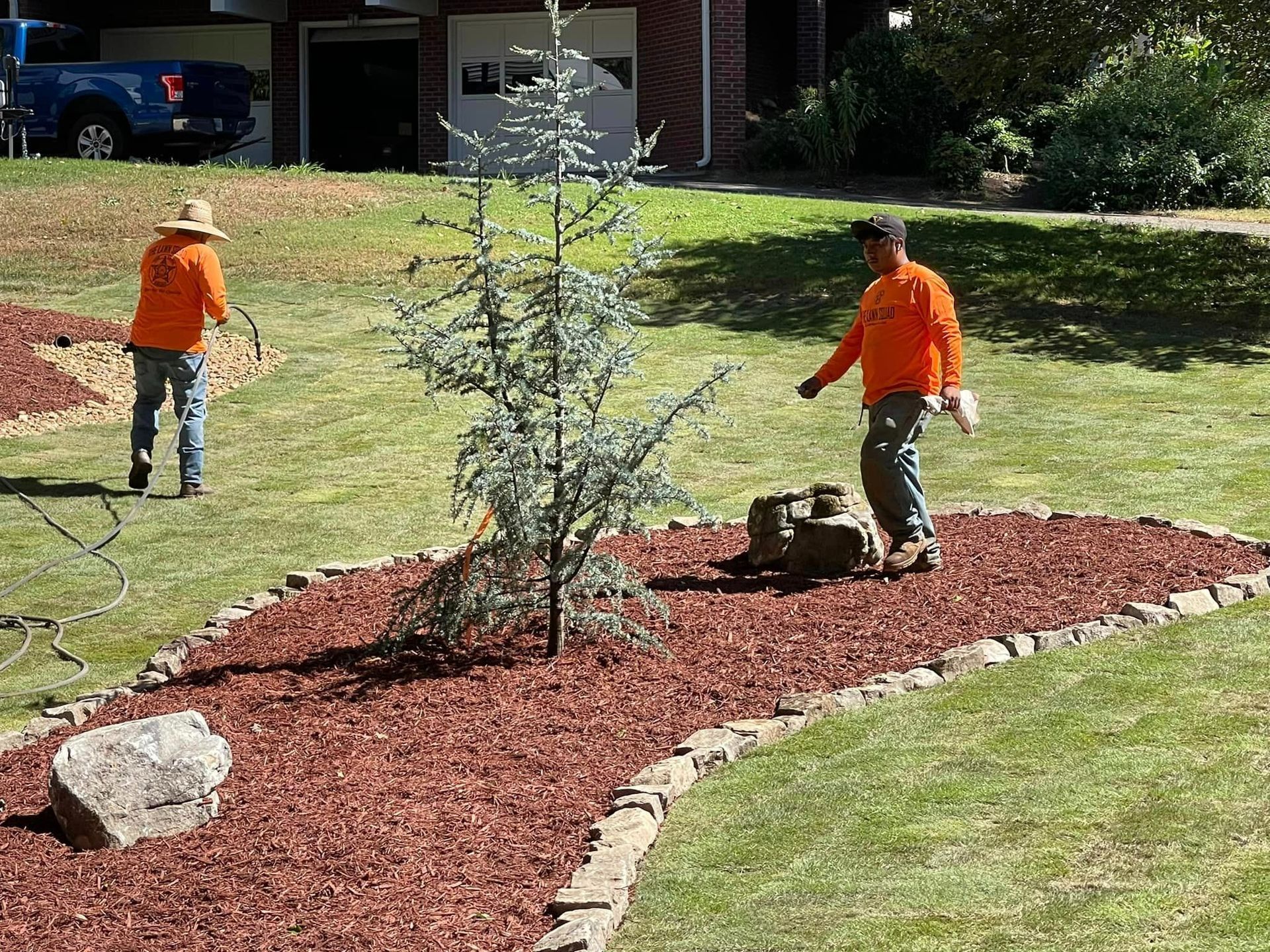 Two men are working on a lawn in front of a house.