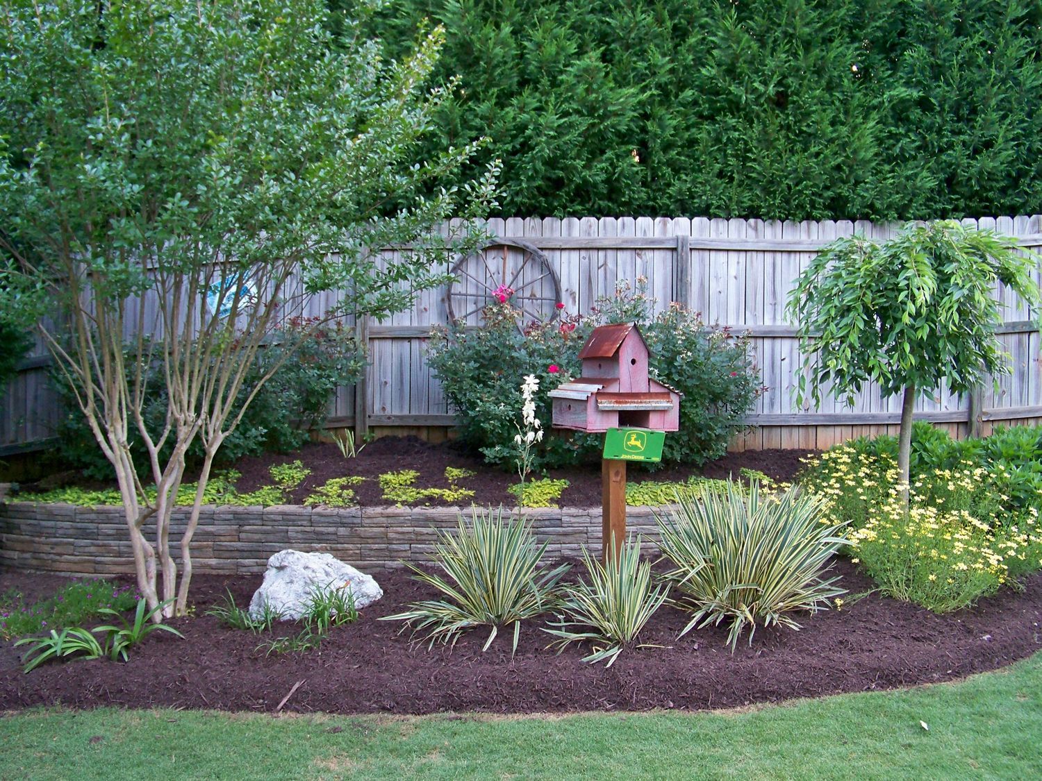 A birdhouse is sitting in the middle of a garden next to a fence.