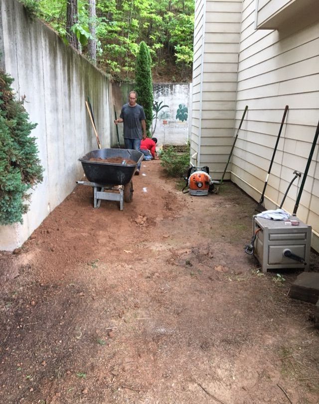 A man is pushing a wheelbarrow full of dirt in a backyard.