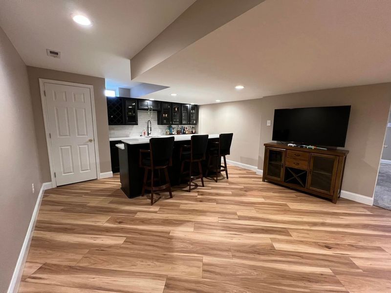 Finished basement with bar, TV on a cabinet, and wood-look flooring.