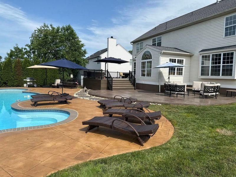 Poolside scene with lounge chairs, umbrellas, and a two-story house.